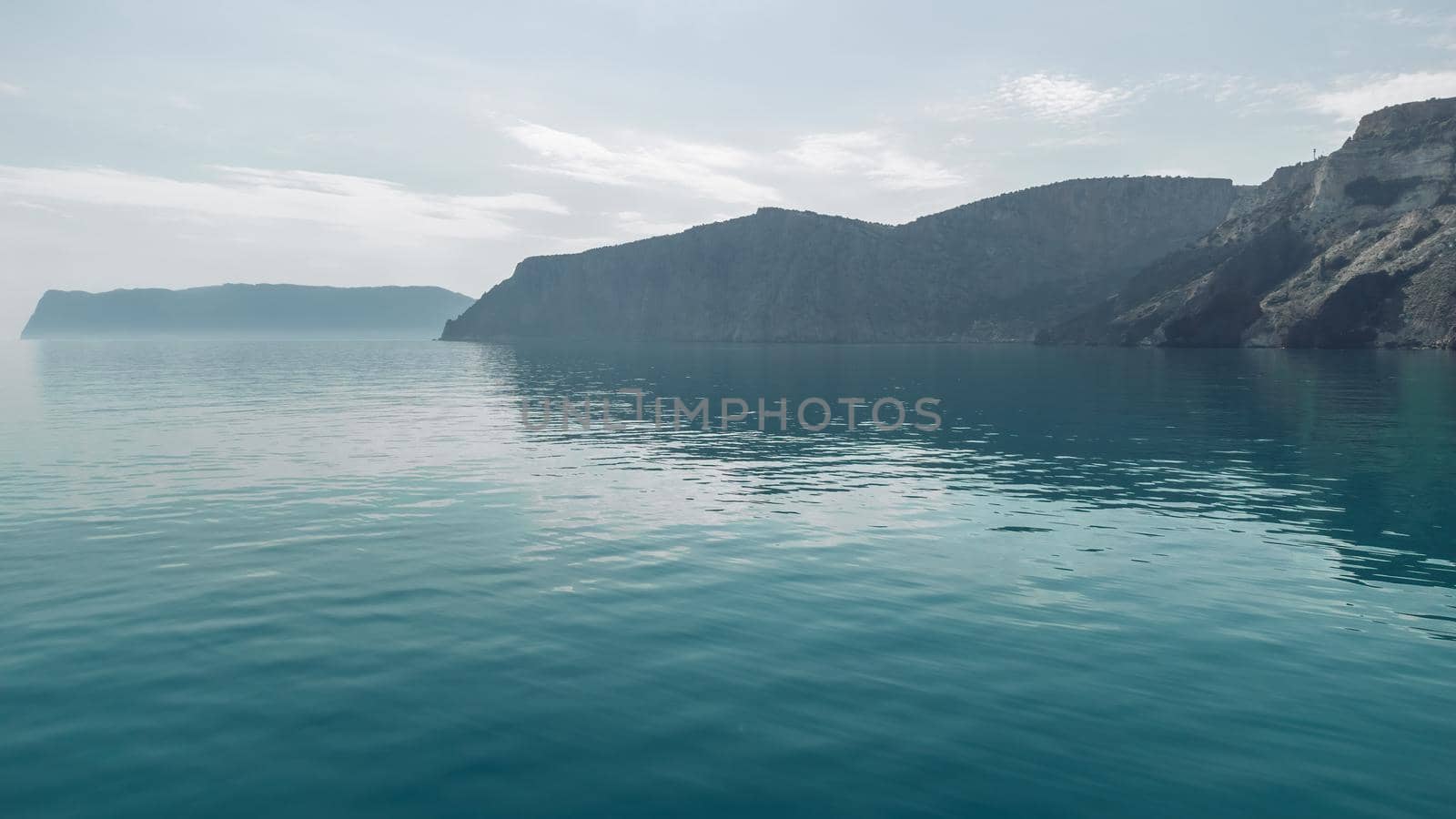 Sea landscape with rocky coastline on sunset time with cloudy sky. Yachts in the Sea on a background of rocky shores. The concept of perfect place for summer travel and rest.