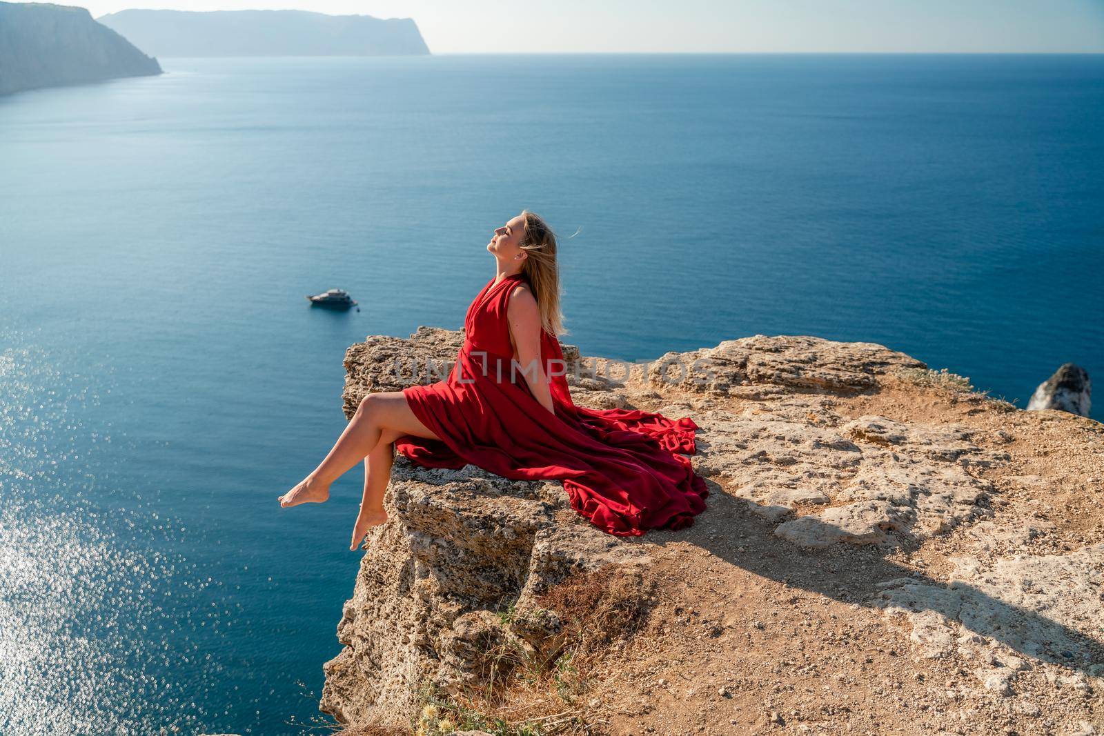 A woman in a red flying dress fluttering in the wind, against the backdrop of the sea