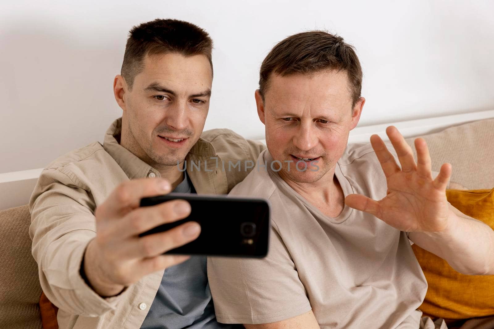 Happy gay couple with casual clothes holding smartphone and talking with friends online, having video call. Homosexual relationships and alternative love