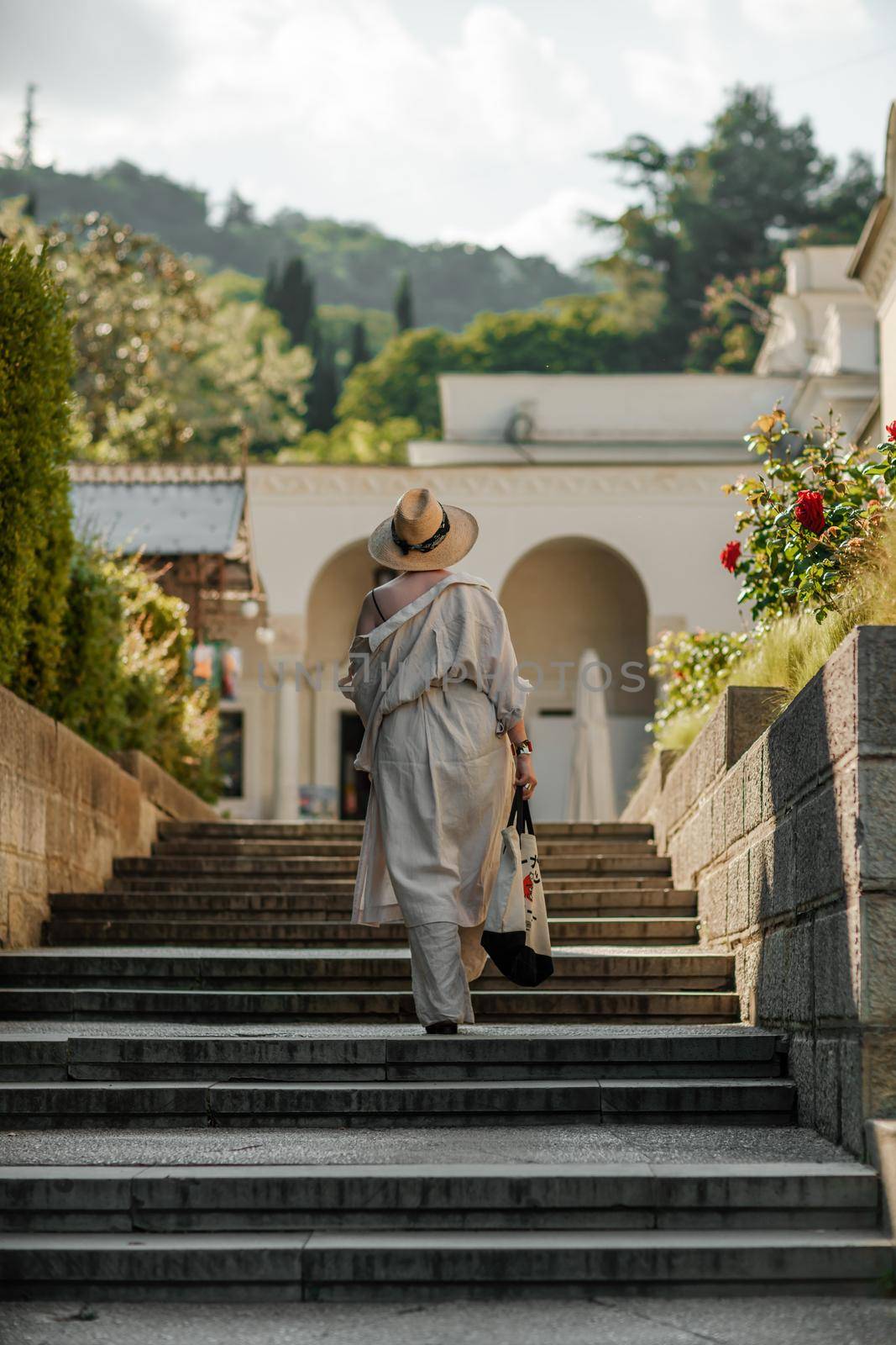 Woman on the stairs in the park. A middle-aged lady in a hat in a white outfit with a bag walks around the Livadia Palace by Matiunina