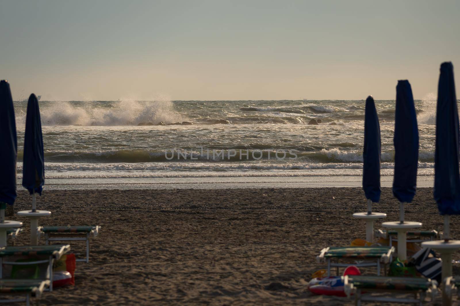 Big waves roll up on the beach. close parasol in bright Sunny day. White foaming waves and splashes.A hot summer day and high wave, seascape.Italy