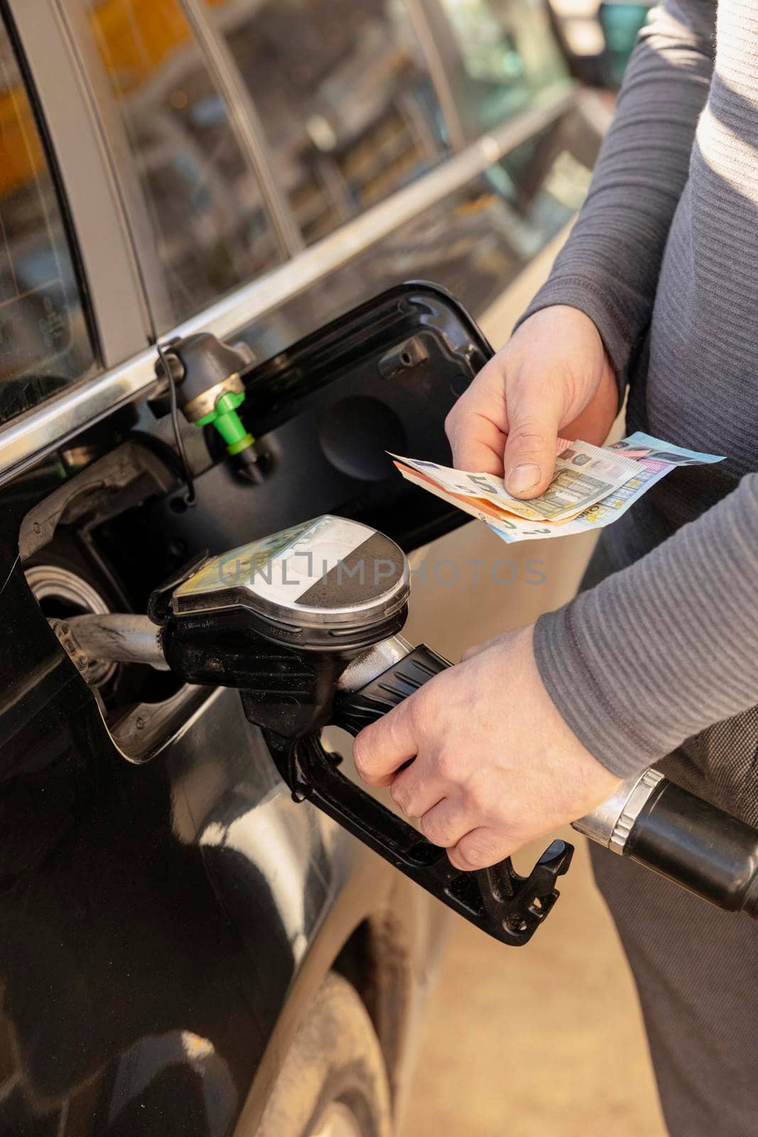 Car refuelling on petrol station. Man refilling car with fuel and holding money, euros. Close up. Gasoline, diesel is getting more expensive. Petrol industry and service. Petrol price and oil crisis