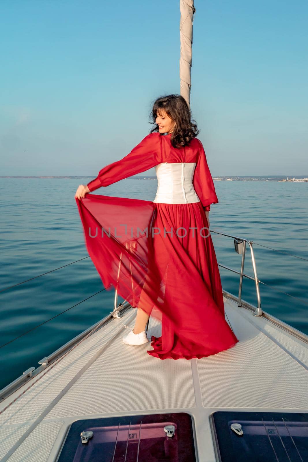 Attractive middle-aged woman in a red dress on a yacht on a summer day. Luxury summer adventure, outdoor activities. by Matiunina