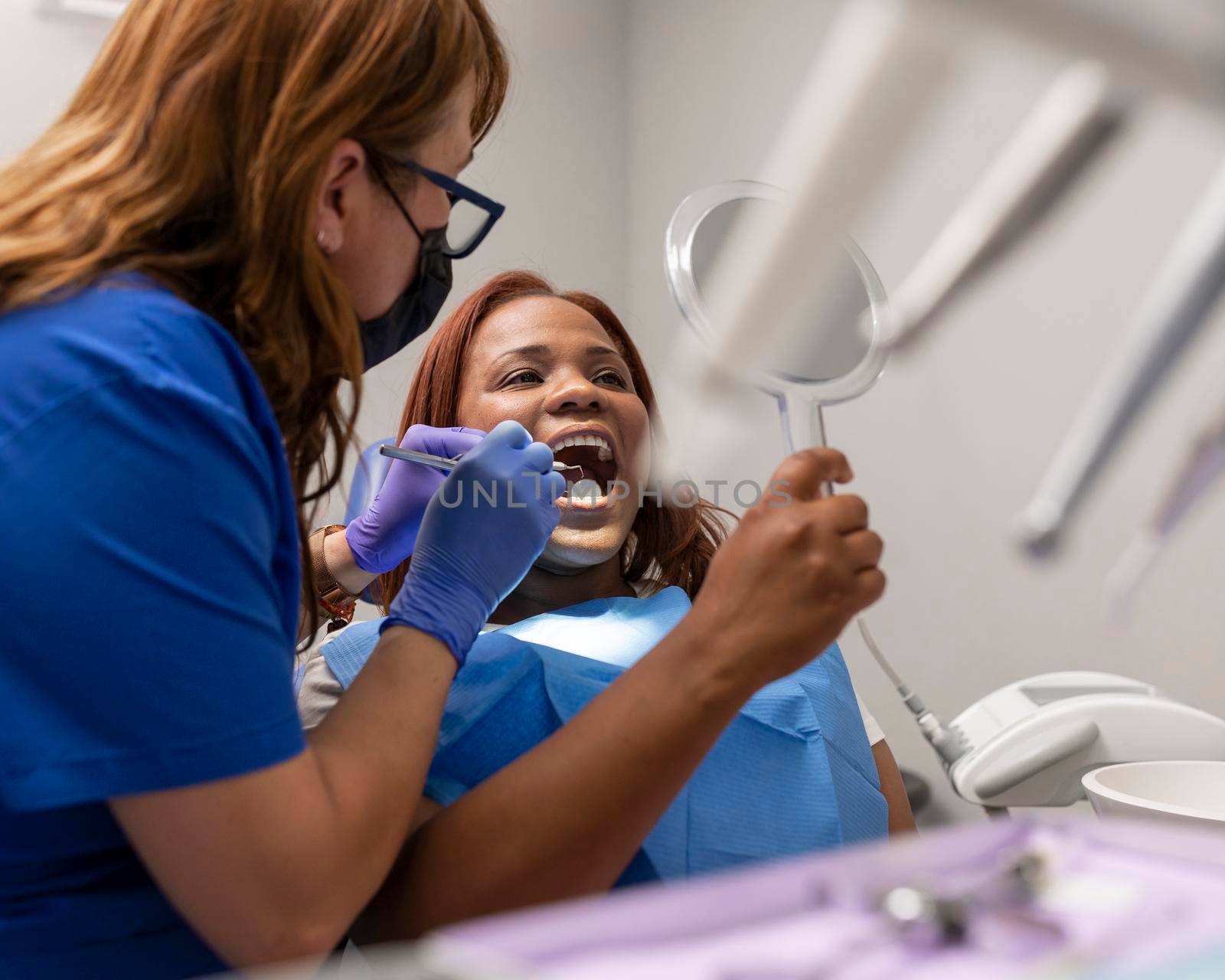 A black woman patient with her mouth open while being treated by her dentist by stockrojoverdeyazul