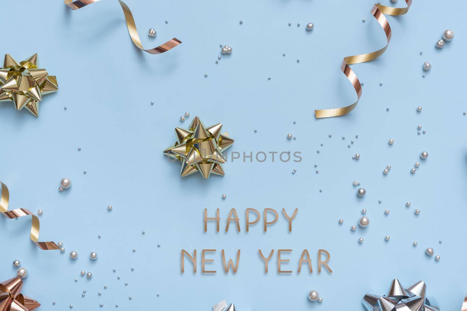Happy new year text on bright festive background with bows and beads top view. New Year greeting background flat lay.