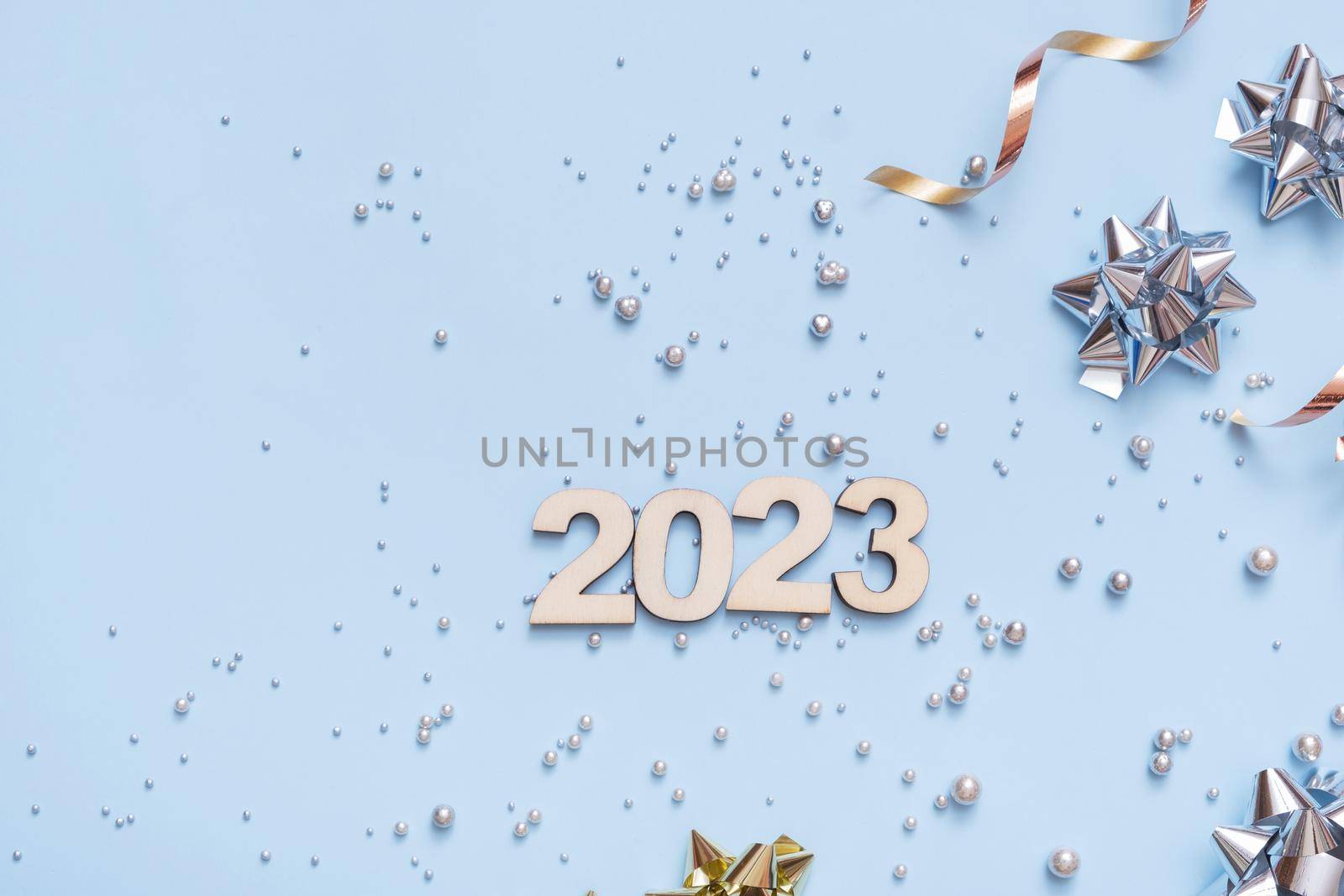 Numbers 2023 on bright festive background with bows and beads top view. New Year background flat lay.