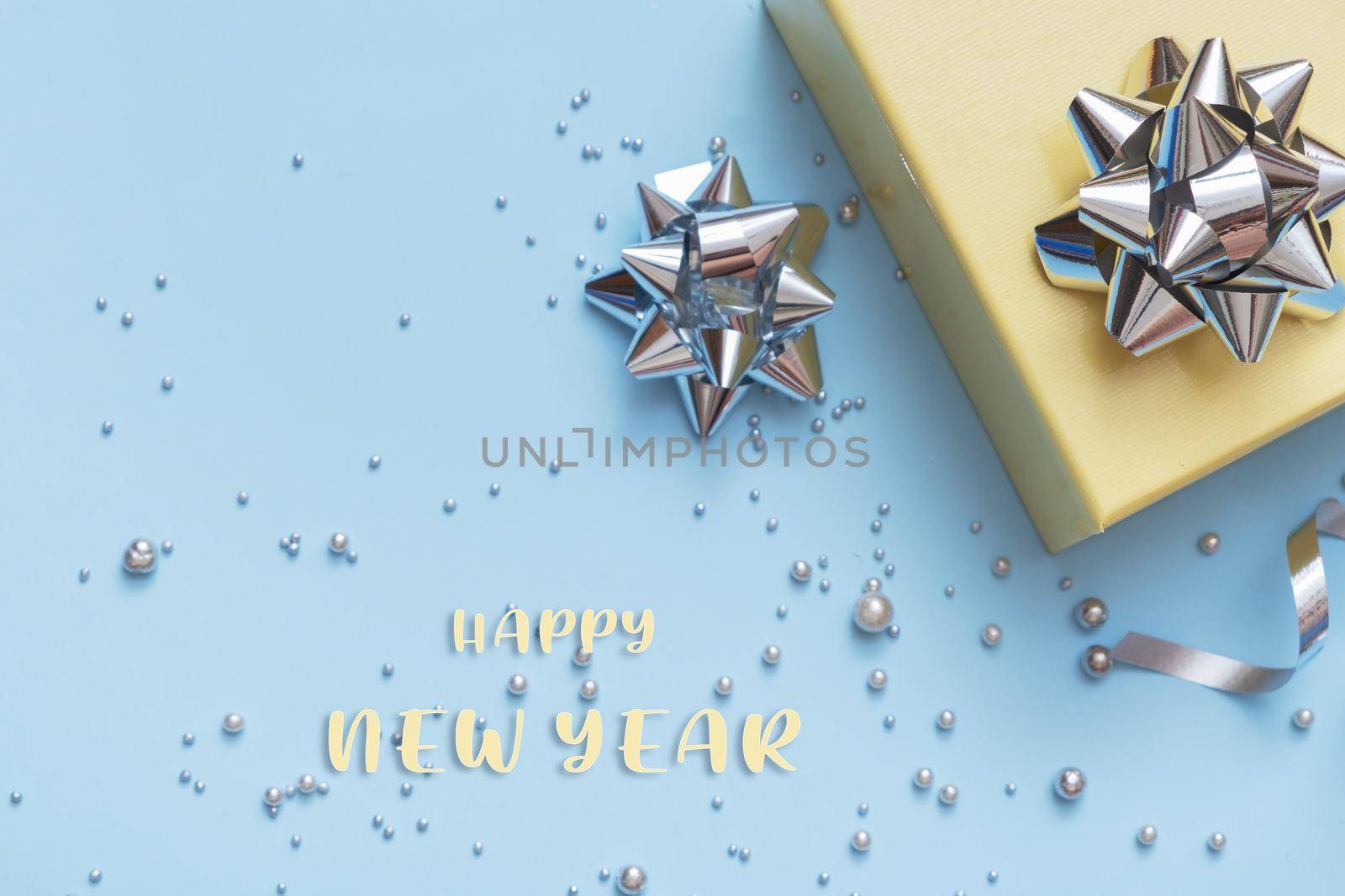 Happy New Year text with gift box, pearls and bows top view on festive blue background by ssvimaliss