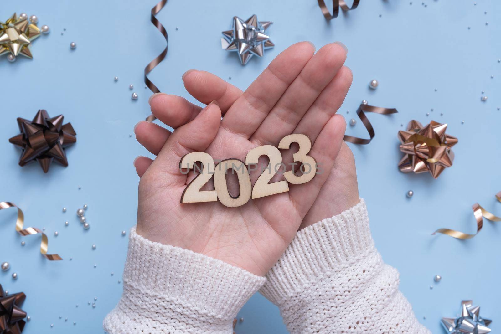 Numbers of the new year 2023 in female hands on a bright festive background with bows and beads top view.