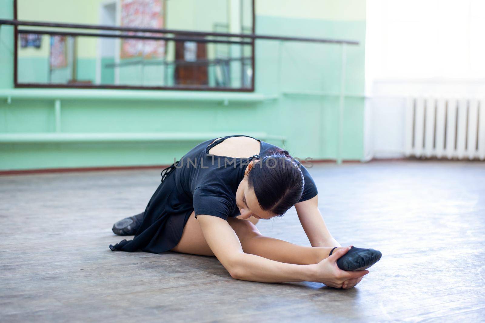 Young brunette female dancer making exercises in ballet studio