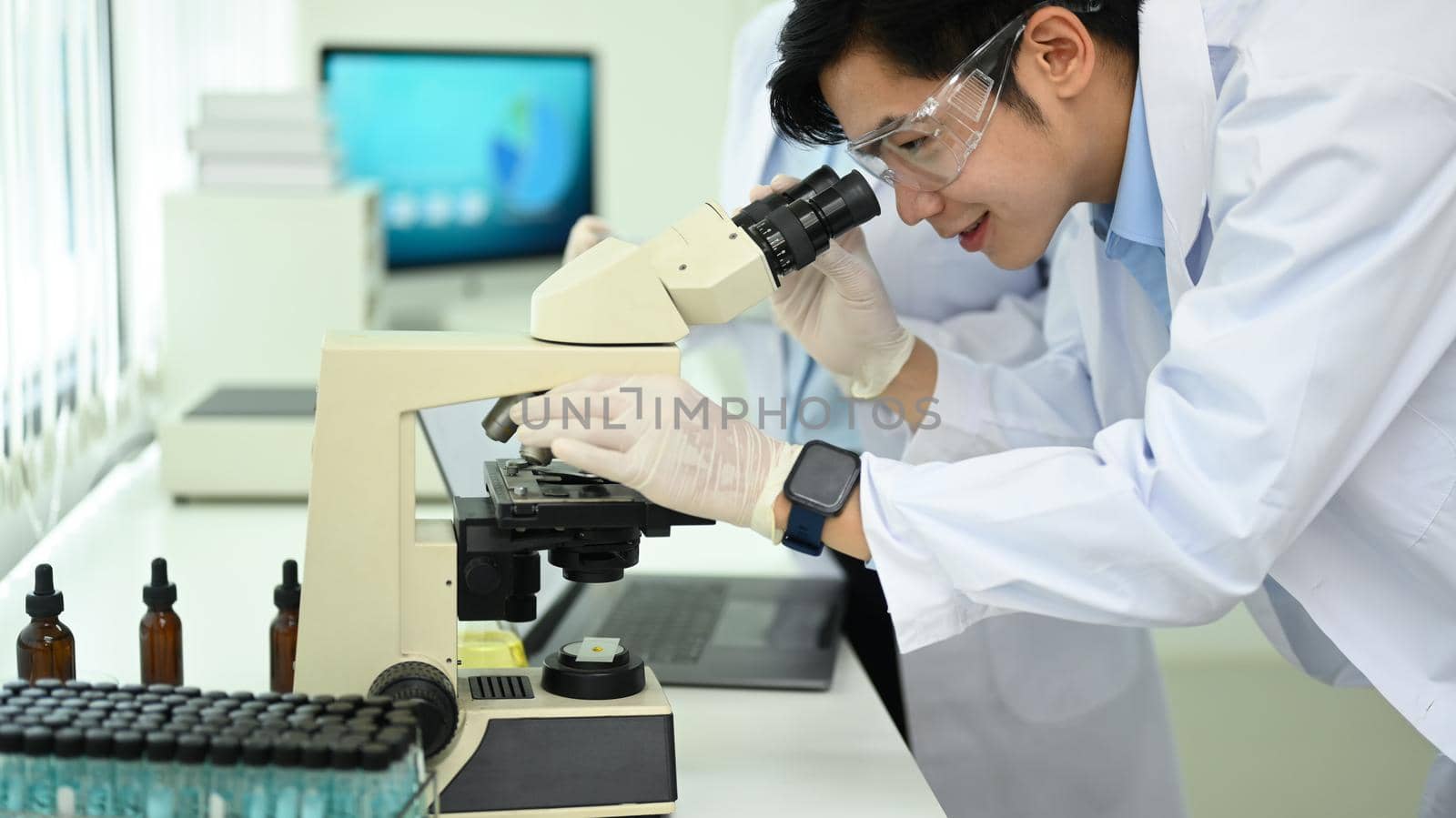Professional biotechnology specialist looking under microscope, conducting experiment in a laboratory.