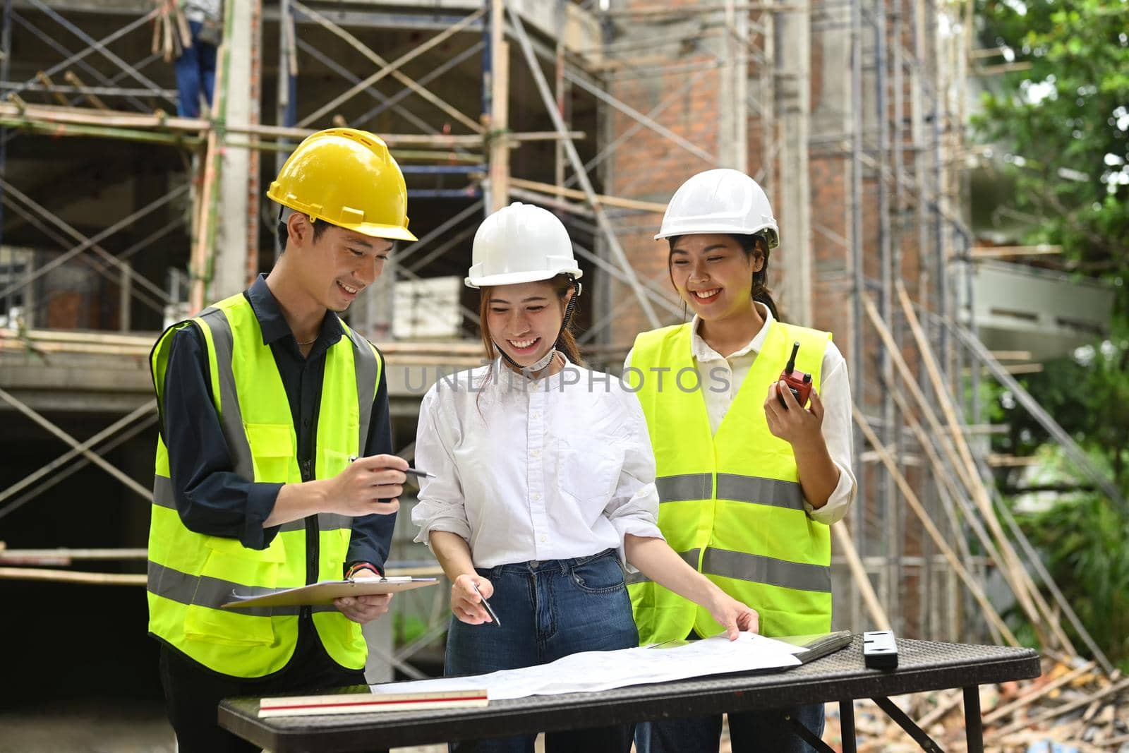 Engineer and specialists wearing safety helmet are discussing work plan, industrial building design project at construction site.