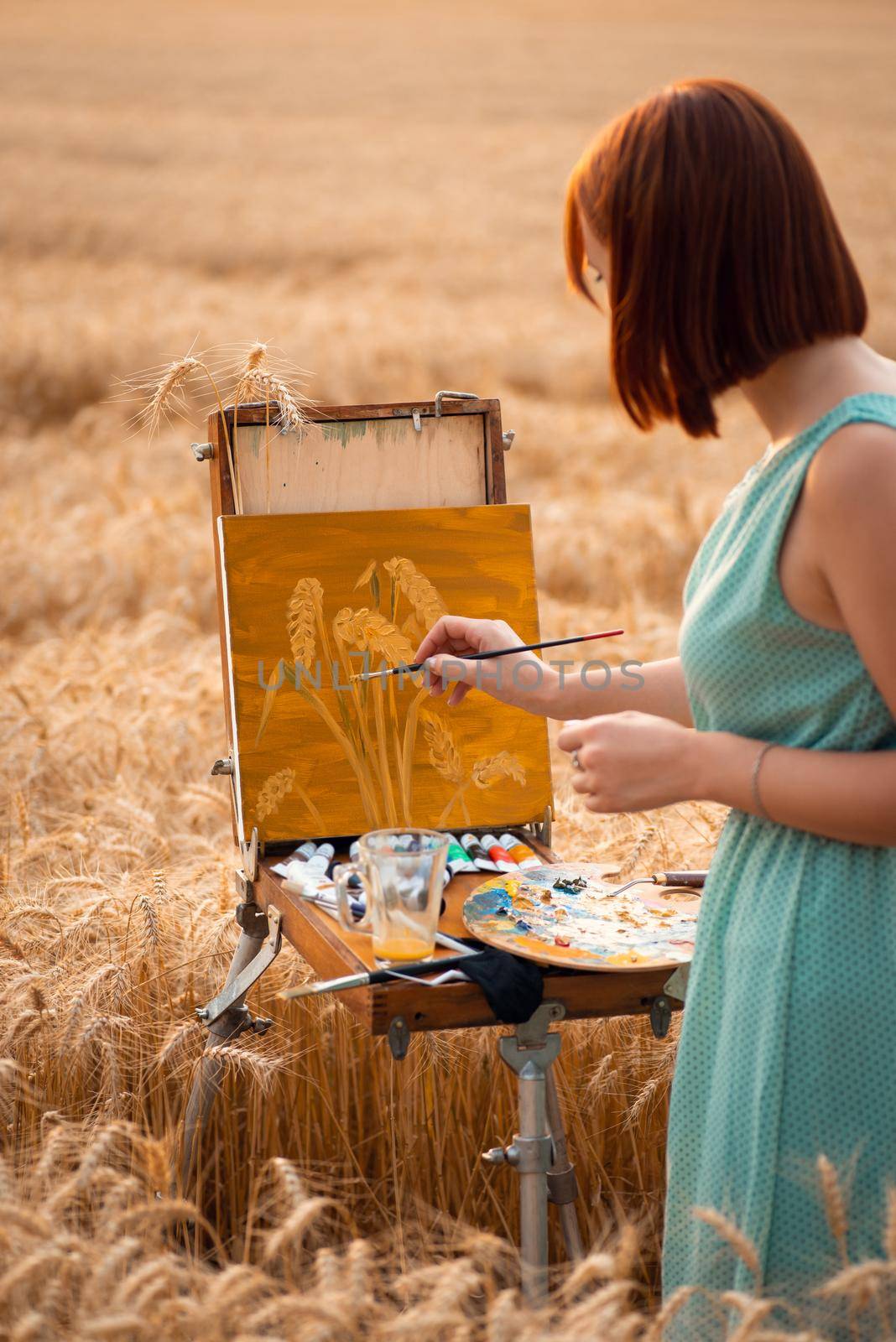 Back view of a professional artist painting spikelets of ripe wheat in the agricultural field