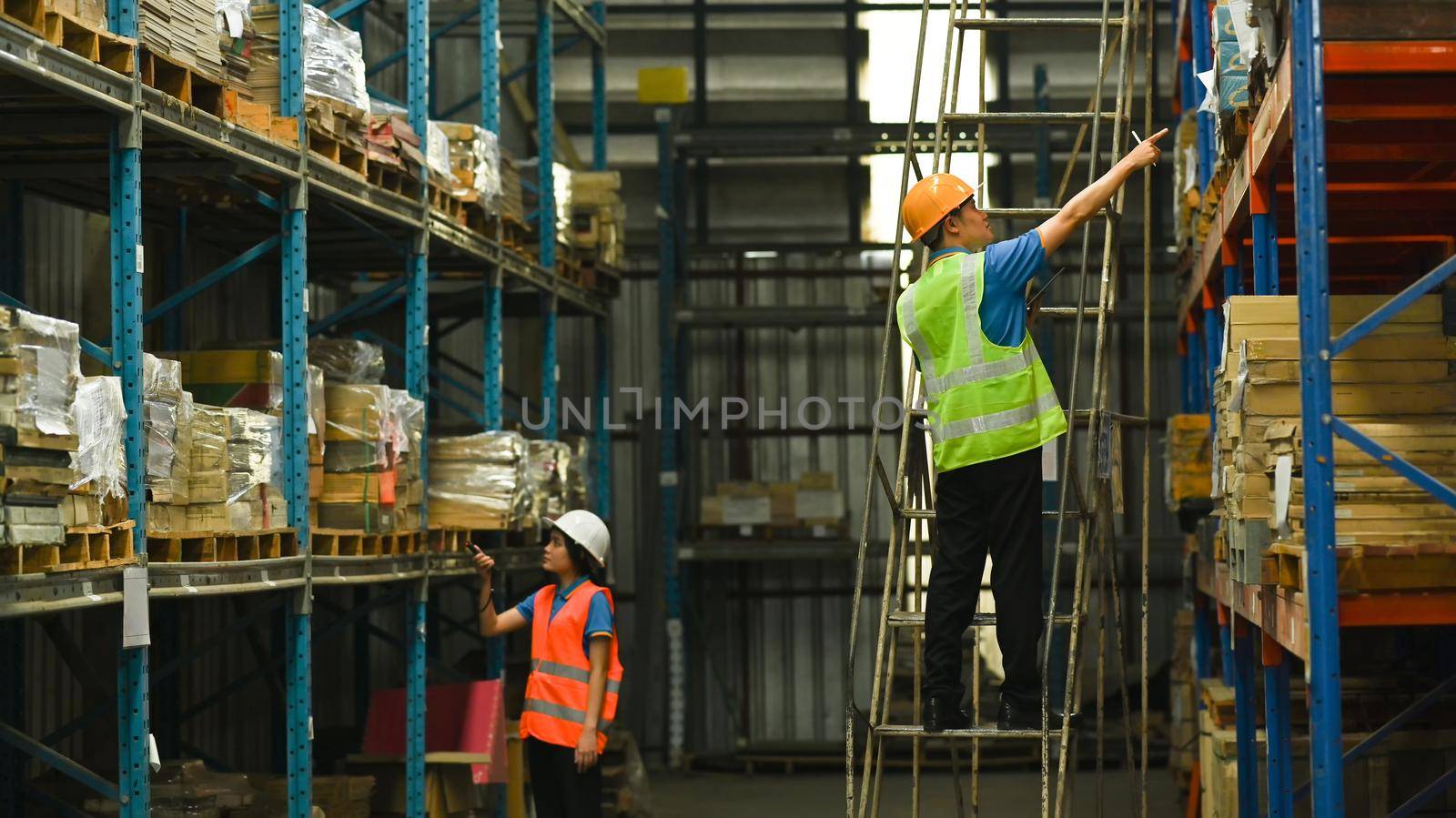 Workers working about shipment in logistic distribution warehouse with tall shelves full of packed boxes and goods.