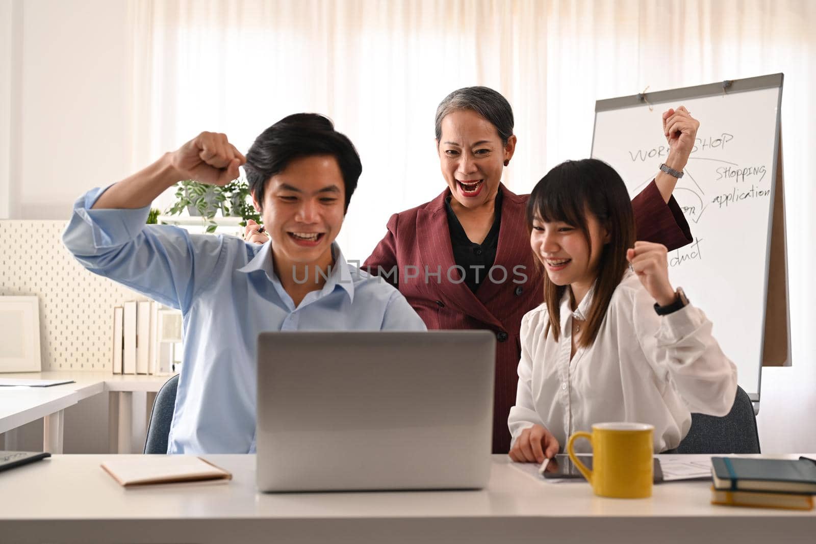 Excited business team looking at laptop screen, celebrating project success or corporate victory at office.
