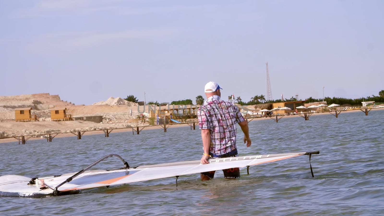 a man pulls the windsurfing board , man learns to ride on a board with a sail, windsurfing on the crystal clear water. High quality photo