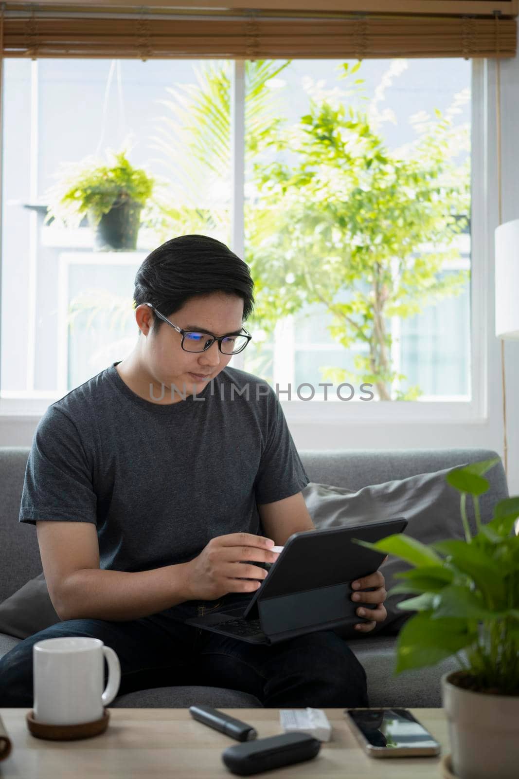 Young asian man working online with computer tablet while sitting on couch.