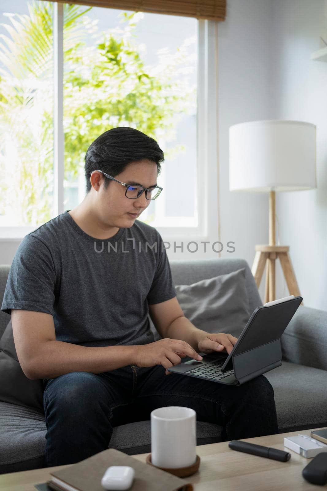 Handsome asian man sitting on sofa and working online with computer tablet. by prathanchorruangsak