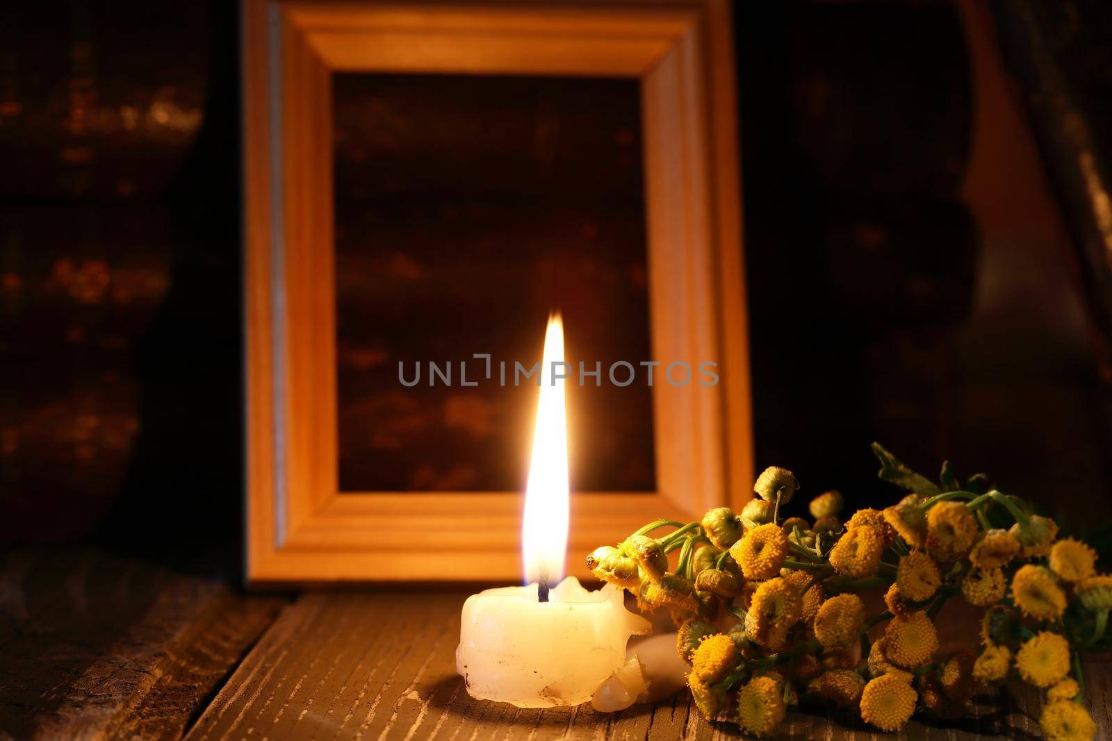 One lighting candle near bunch of wild flowers against free picture frame