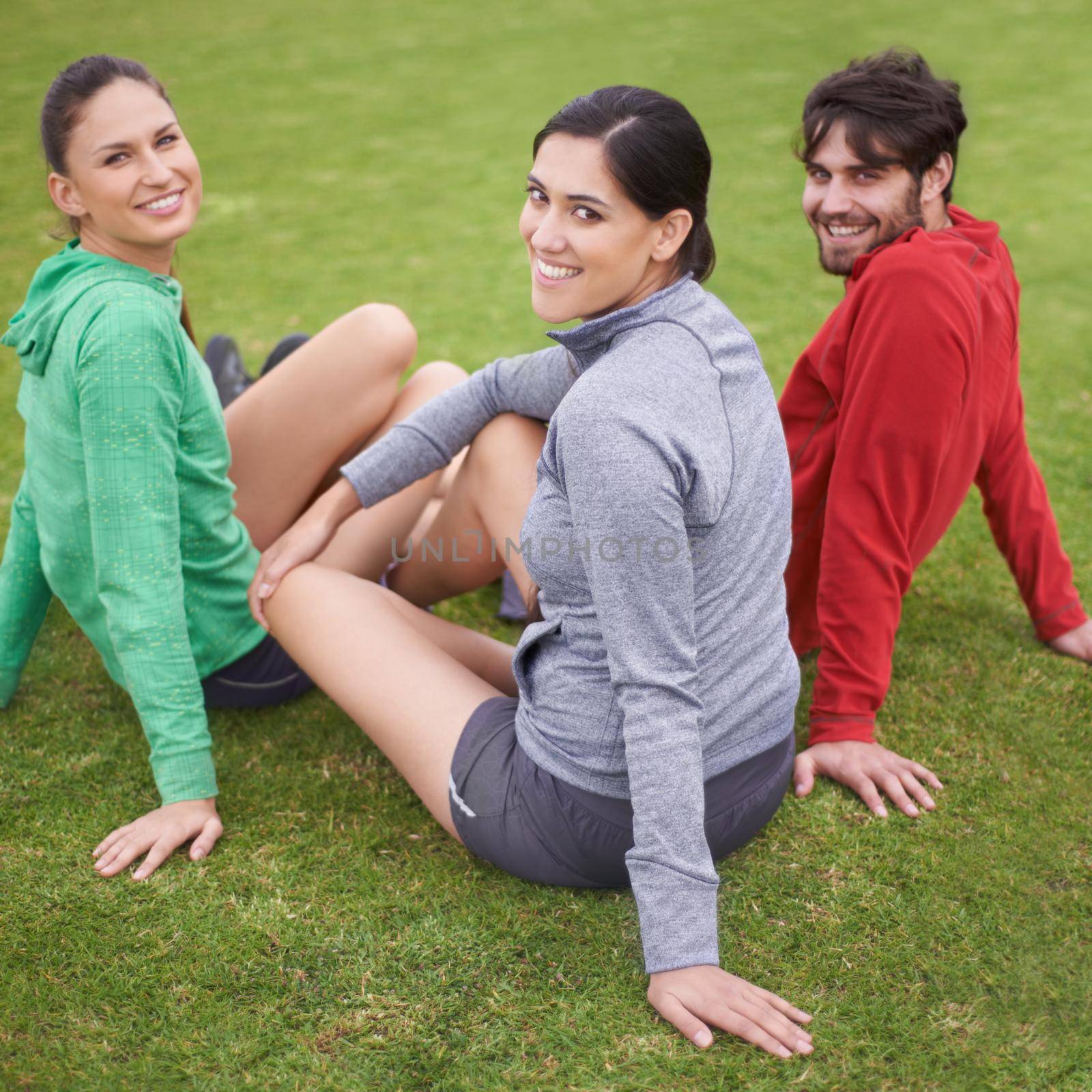 Looking great and we know it. Portrait of young people in exercise clothing sitting on a grassy sports field. by YuriArcurs