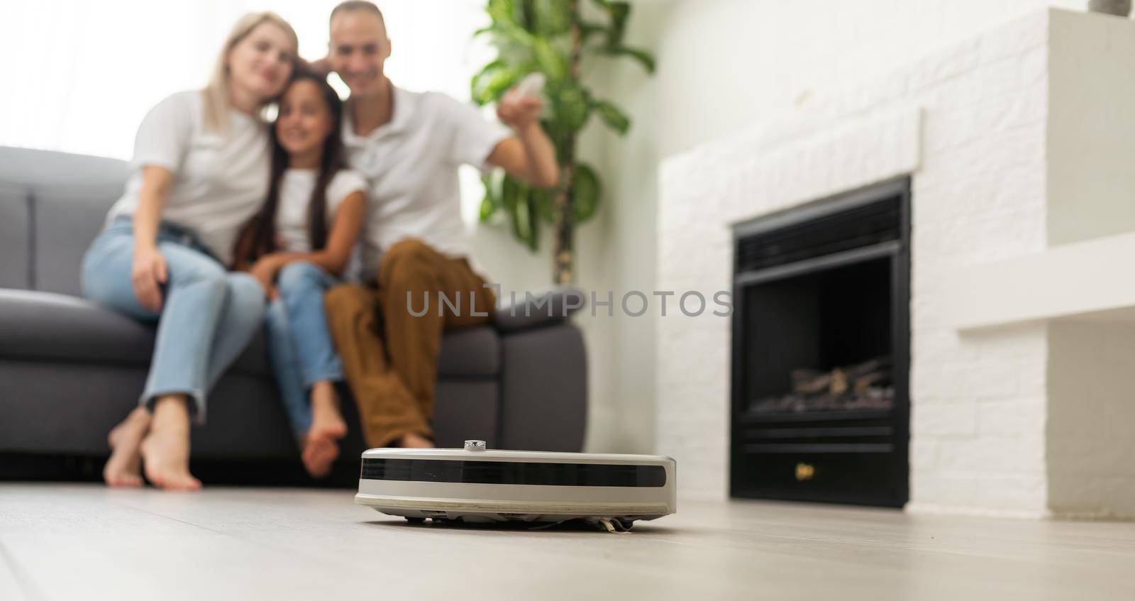 Family resting while robotic vacuum cleaner doing its work at home.