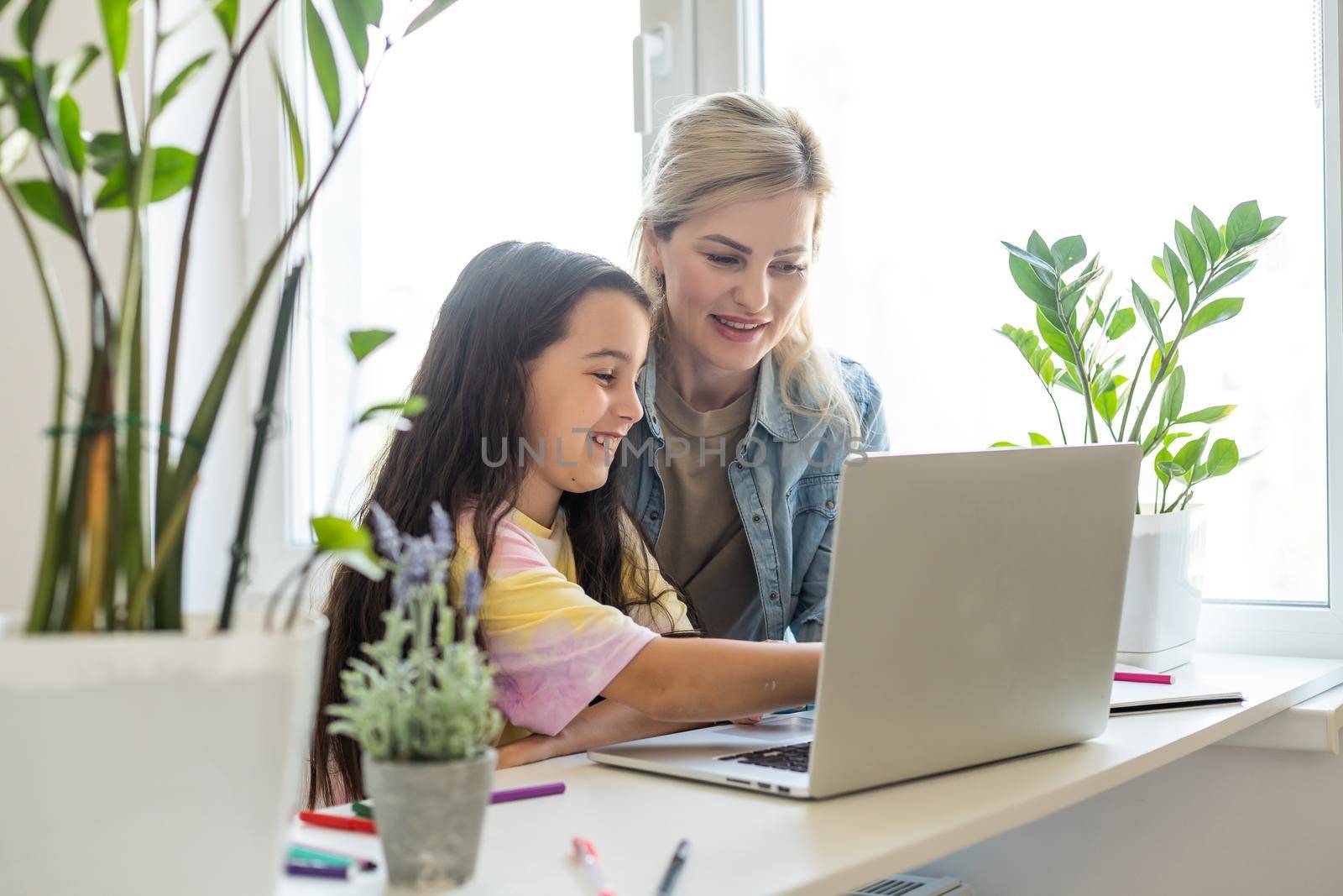 Beautiful mother and child looks at laptop screen spend time in kitchen using app education program, choose cartoons, teach kid pc usage, controls what daughter watching on internet cyberspace concept