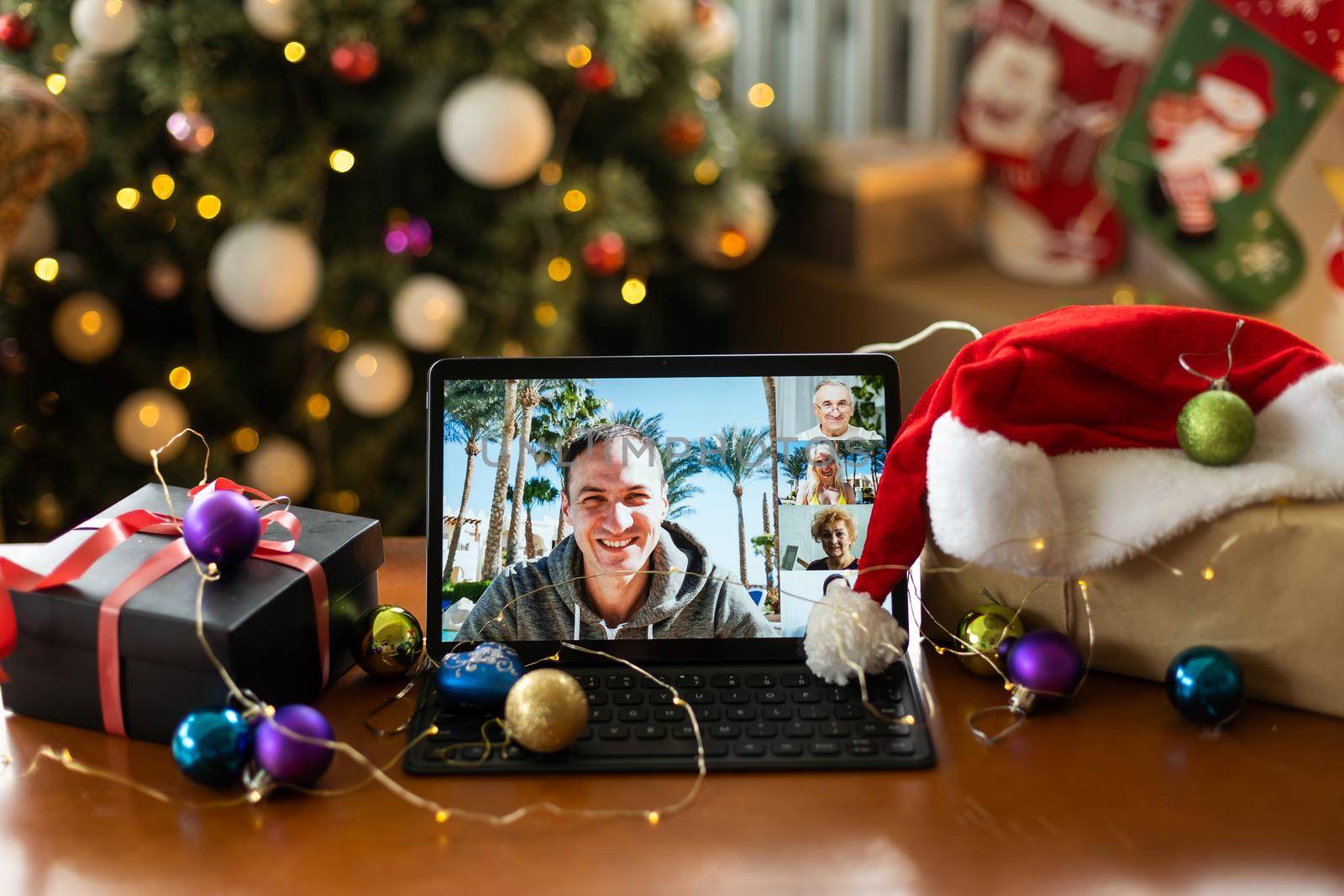 Smiling handsome young man enjoys decorating the Christmas tree while holding a tablet for video call or a selfie at home. Celebrating the New Year alone by Andelov13