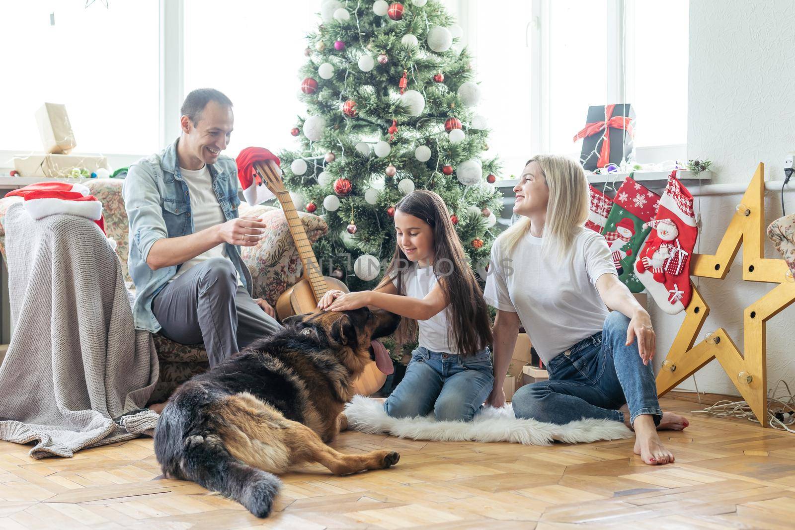 Merry Christmas and Happy New Year. Happy family with dog are waiting for the New Yearwhile sitting near beautiful Christmas tree at home