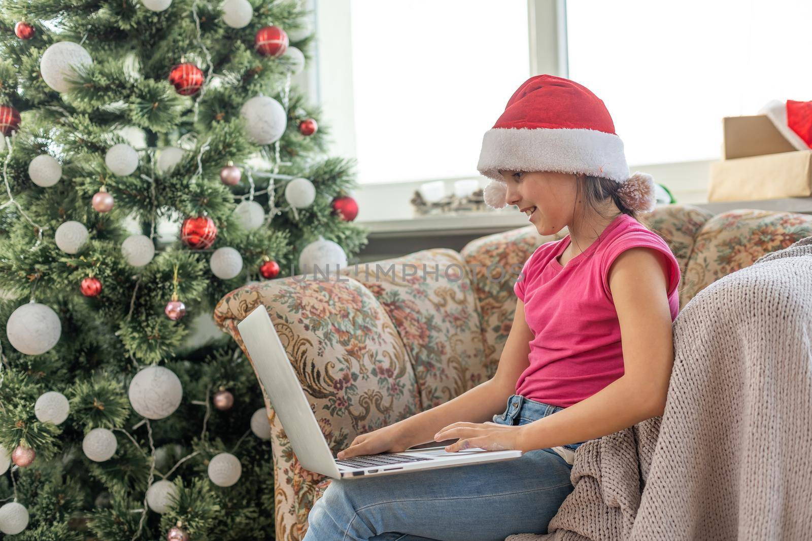 winter holidays, technology and children concept - little student girl with laptop computer at home over christmas tree background