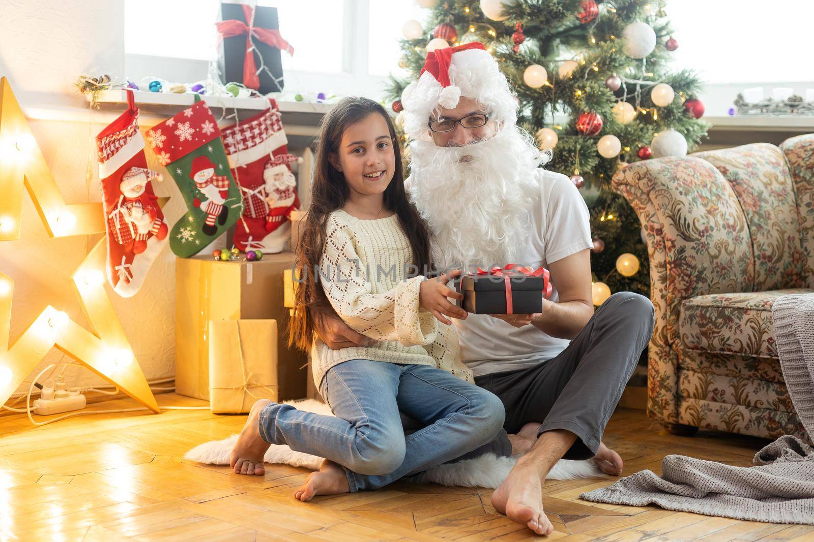 Picture of happy family celebrating New Year eve, little girl with parents enjoying winter holidays, father wearing Santa Claus costume, Christmas magic, happiness and love concept.