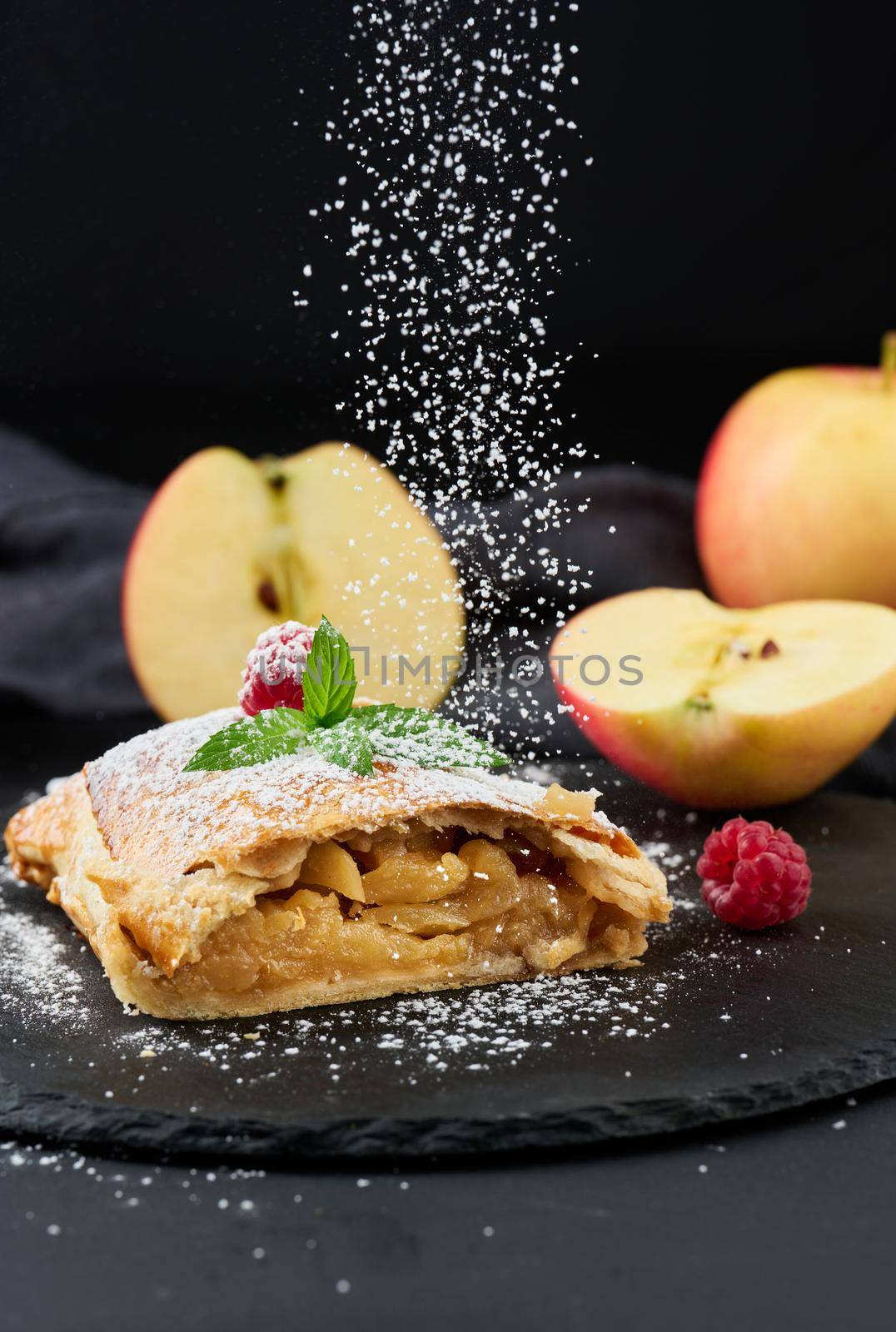 Baked strudel with apples sprinkled with powdered sugar on a black board, delicious dessert