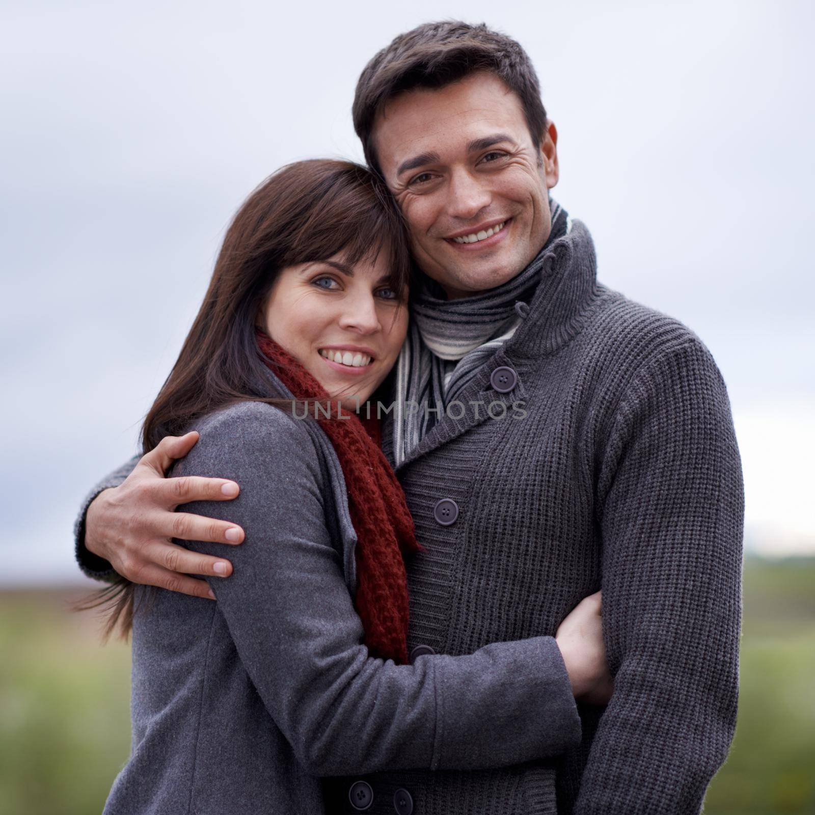 Their love is evident to all. A young couple embracing while standing outside. by YuriArcurs