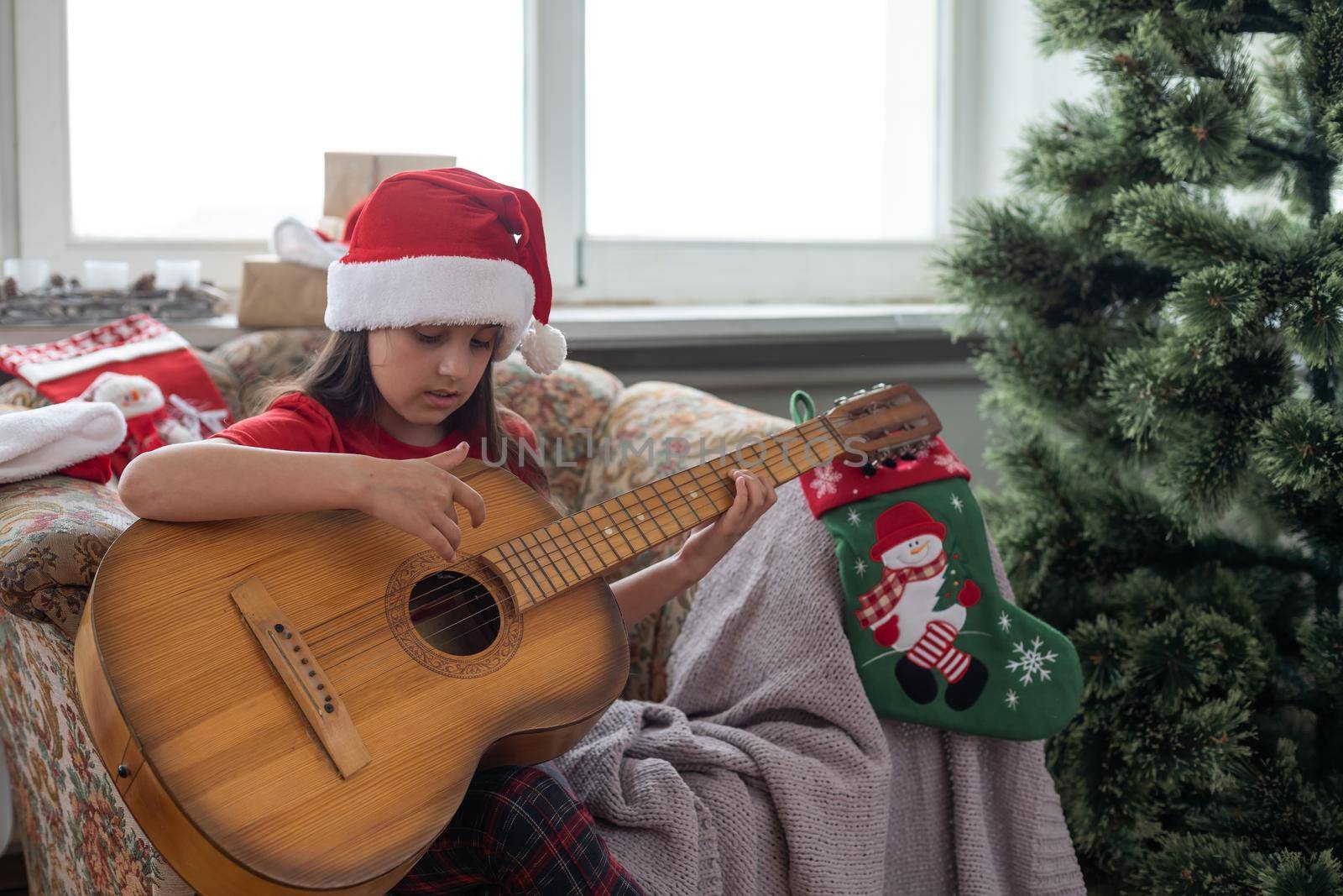 Child playing the guitar and singing near a christmas tree.