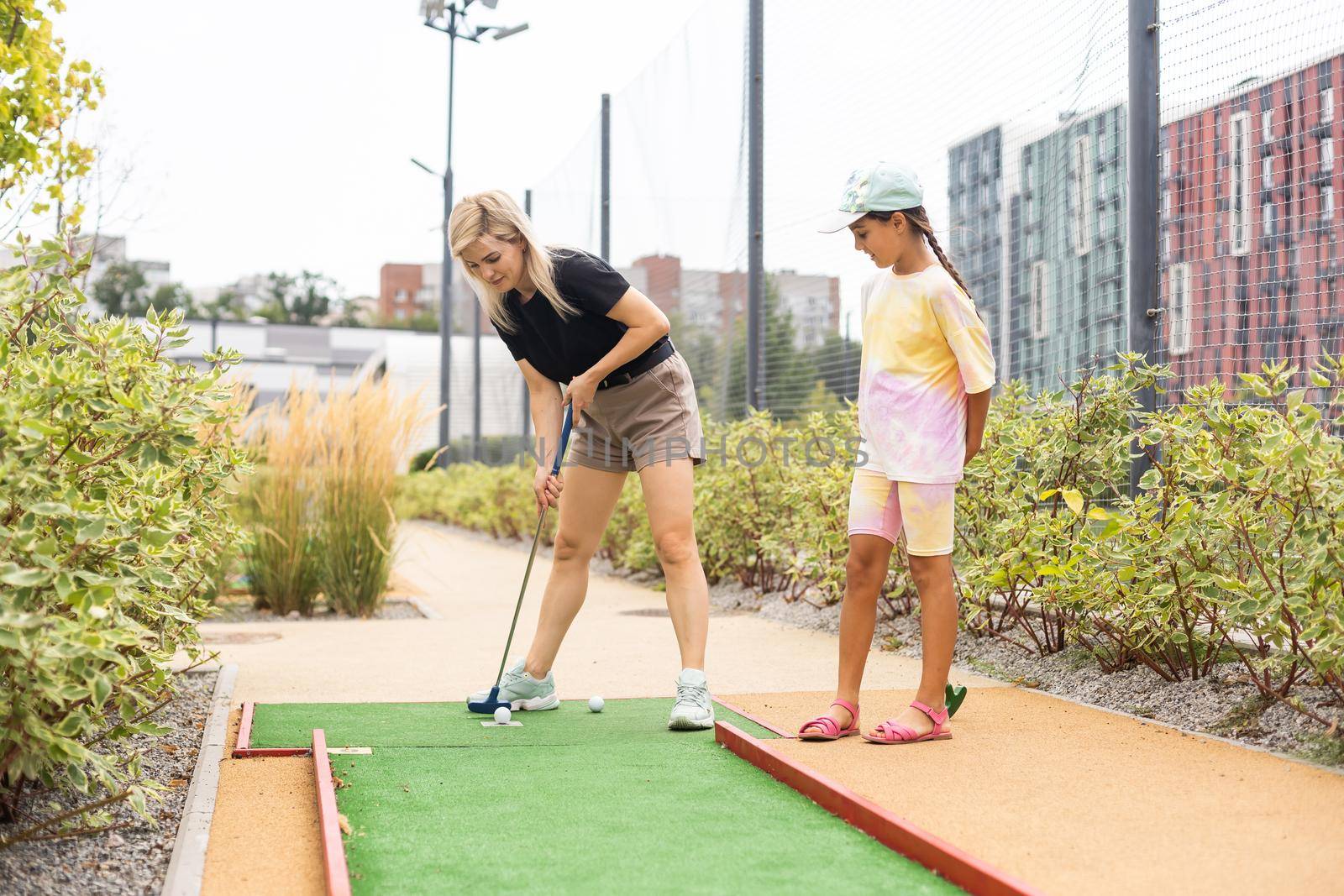 Detail of young woman and daughter playing mini adventure golf on a beautiful sunny summer day by Andelov13