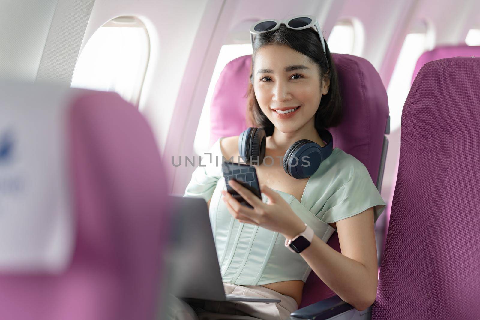 Joyful asian woman sits in the airplane and using mobile phone while go to travel.