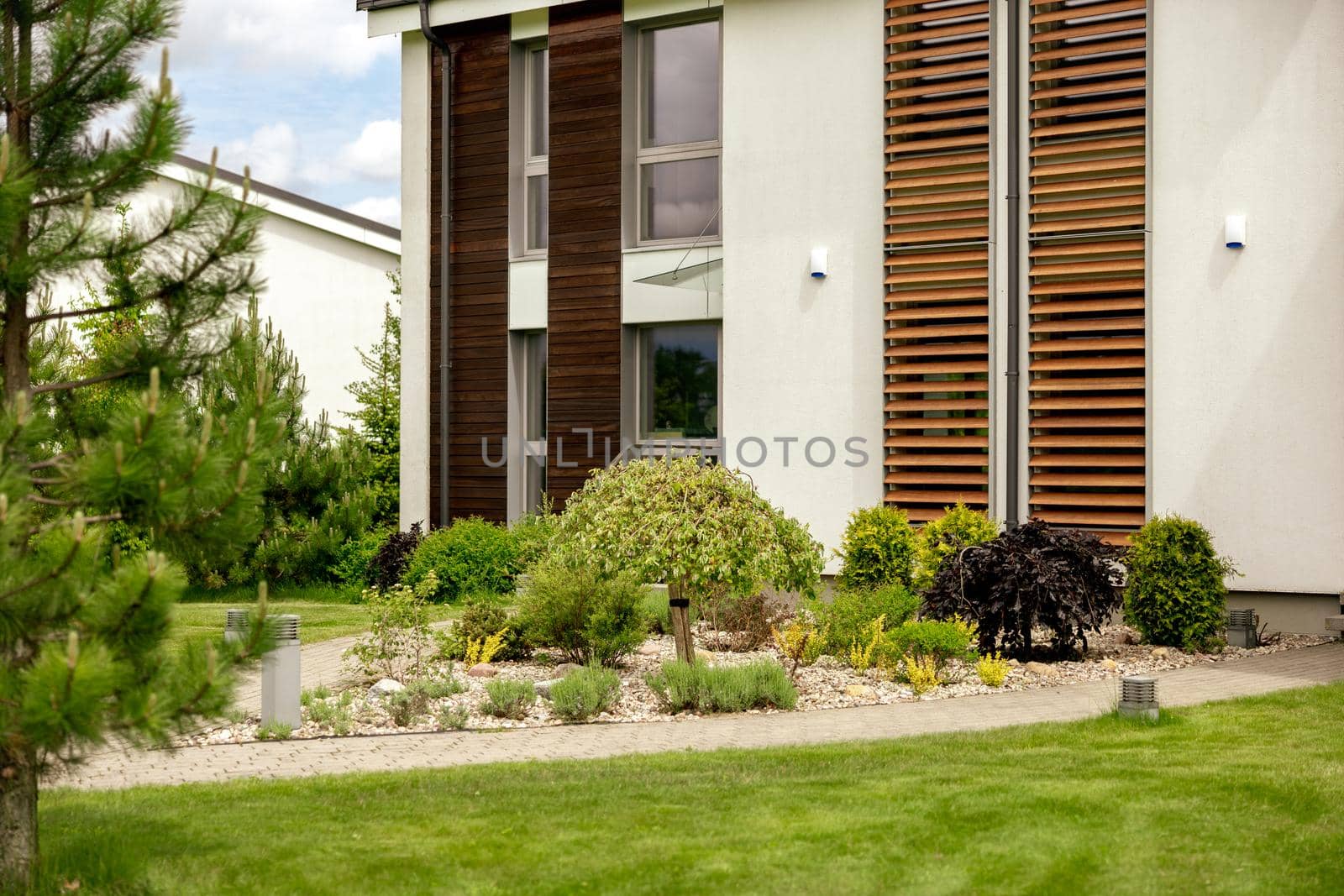 Various plants and stones in front of modern house, front yard. Landscape design. Beautiful garden. Modern urban living residences with private courtyards. Green outdoor facilities, lawn. Garden care