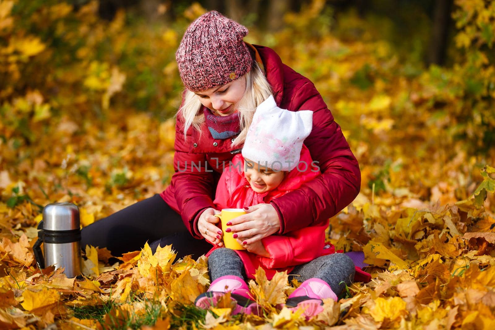 Hello autumn. smiling young mother and daughter in hats outdoors in the city park in autumn having fun time. by Andelov13