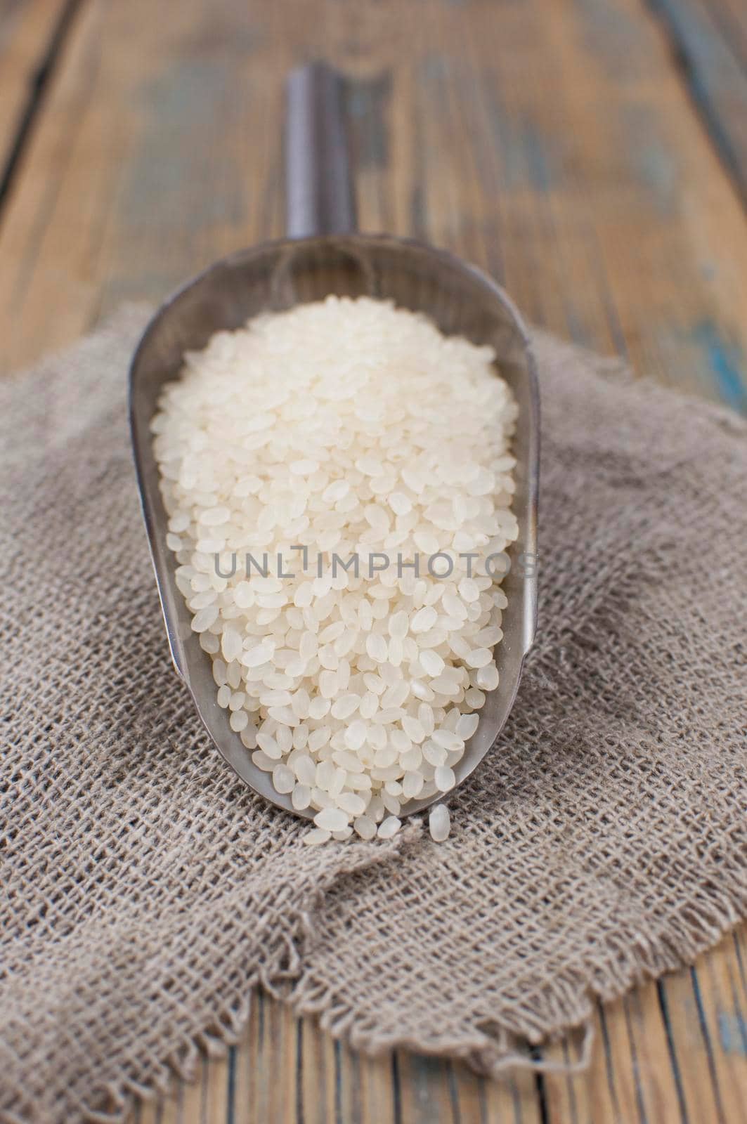 White uncooked, raw grain rice in metal scoop on rustic  wooden table, top view, flat lay, from above