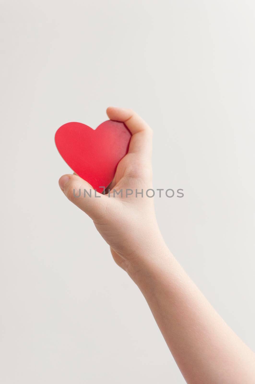 Baby's hand holding a red heart over white wall background 