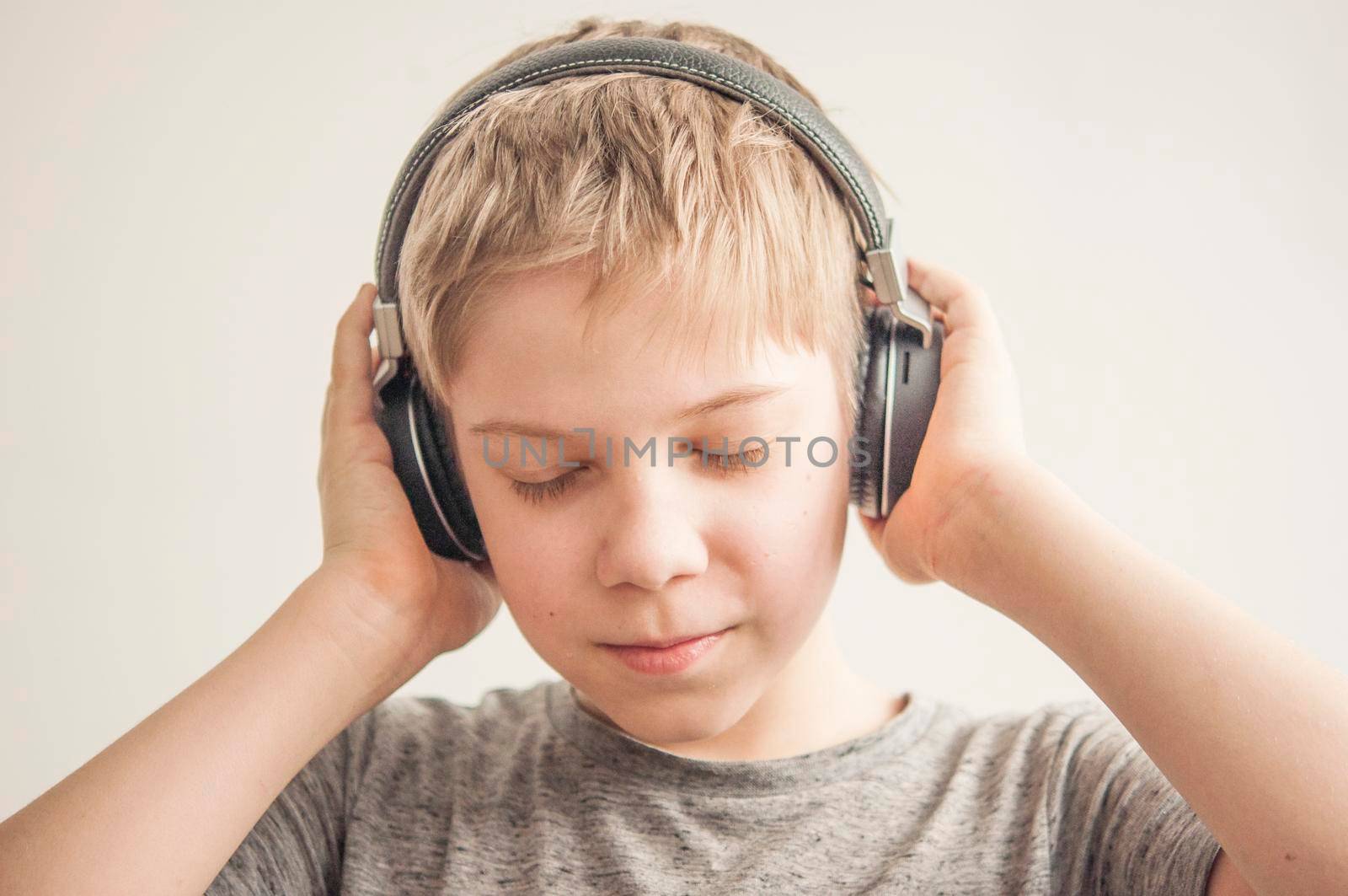 Stylish teen boy listening music in headphones and singing against white background. School child listening loud music in wireless earphones