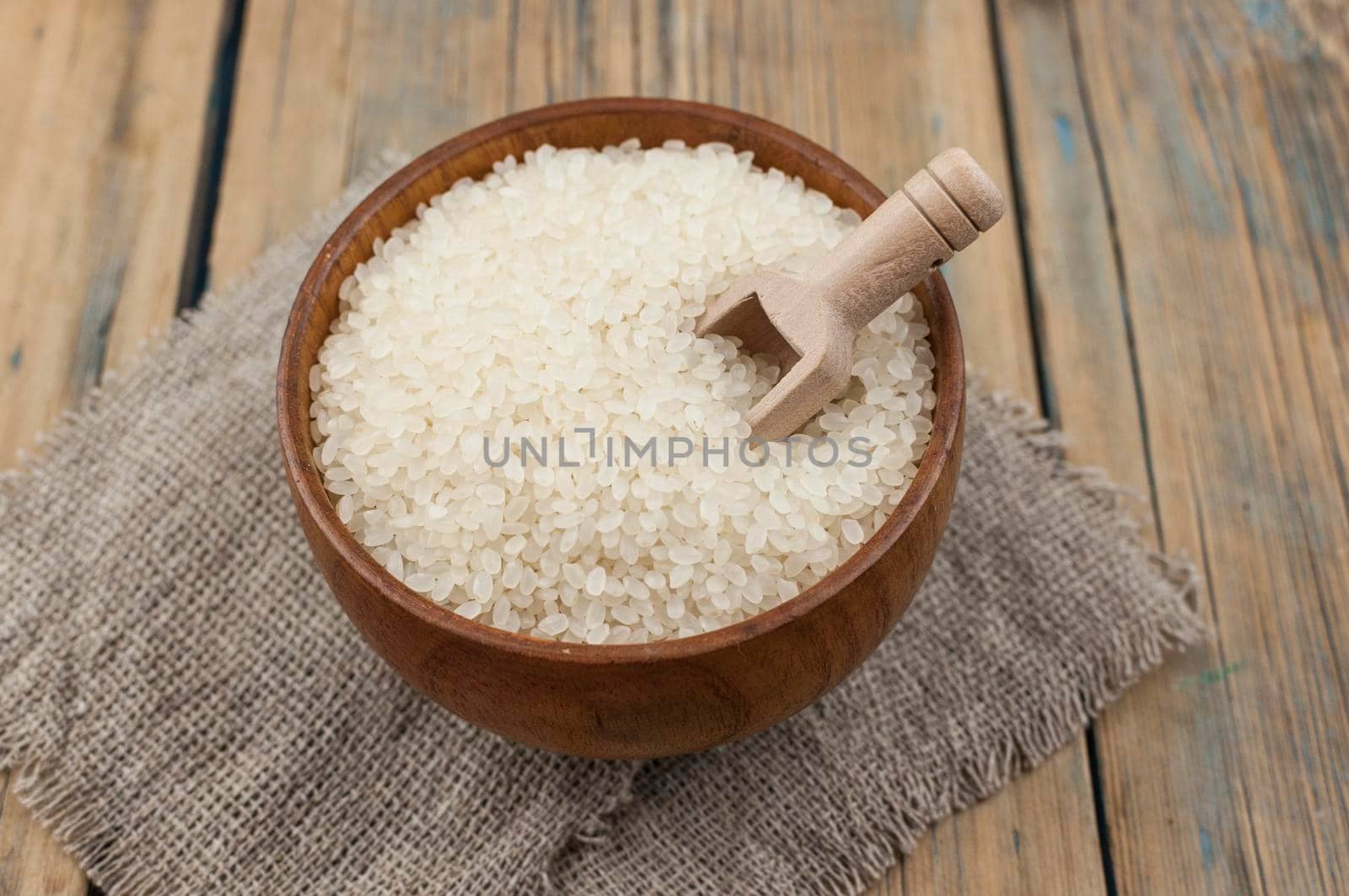 raw white sticky rice in wood bowl with wood spoon on gunny sack cloth on wooden table, top view with copy space