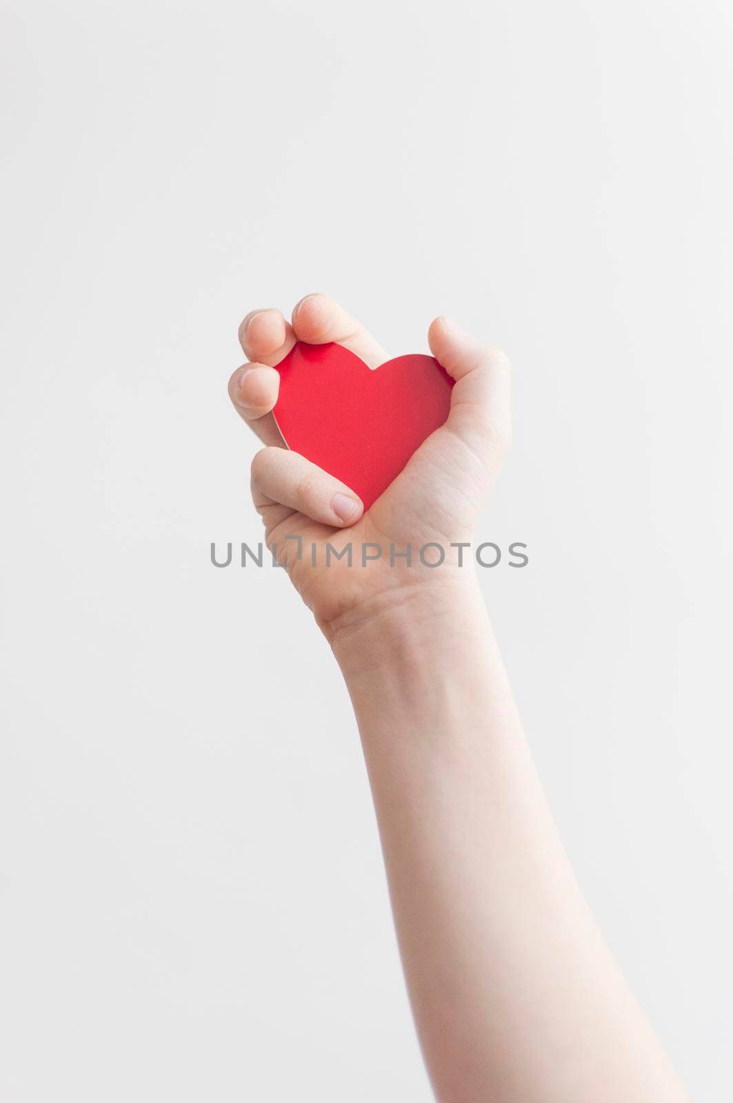 Baby's hand holding a red heart over white wall background 