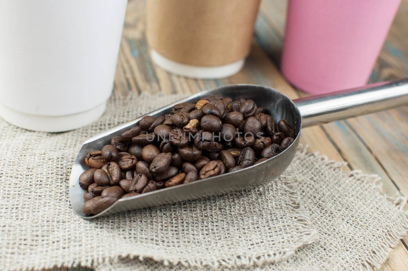 Disposable take-out mockup paper cups with coffee beans for morning espresso and spoon in brown bowl on wooden background