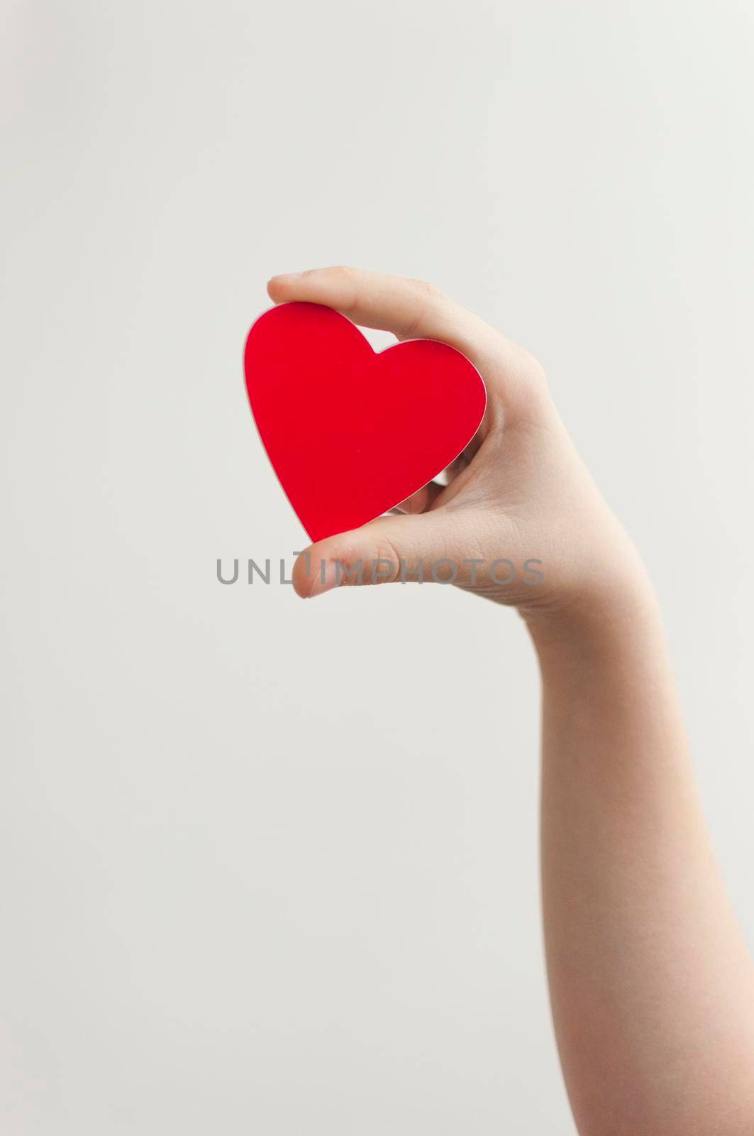 Baby's hand holding a red heart over white wall background 
