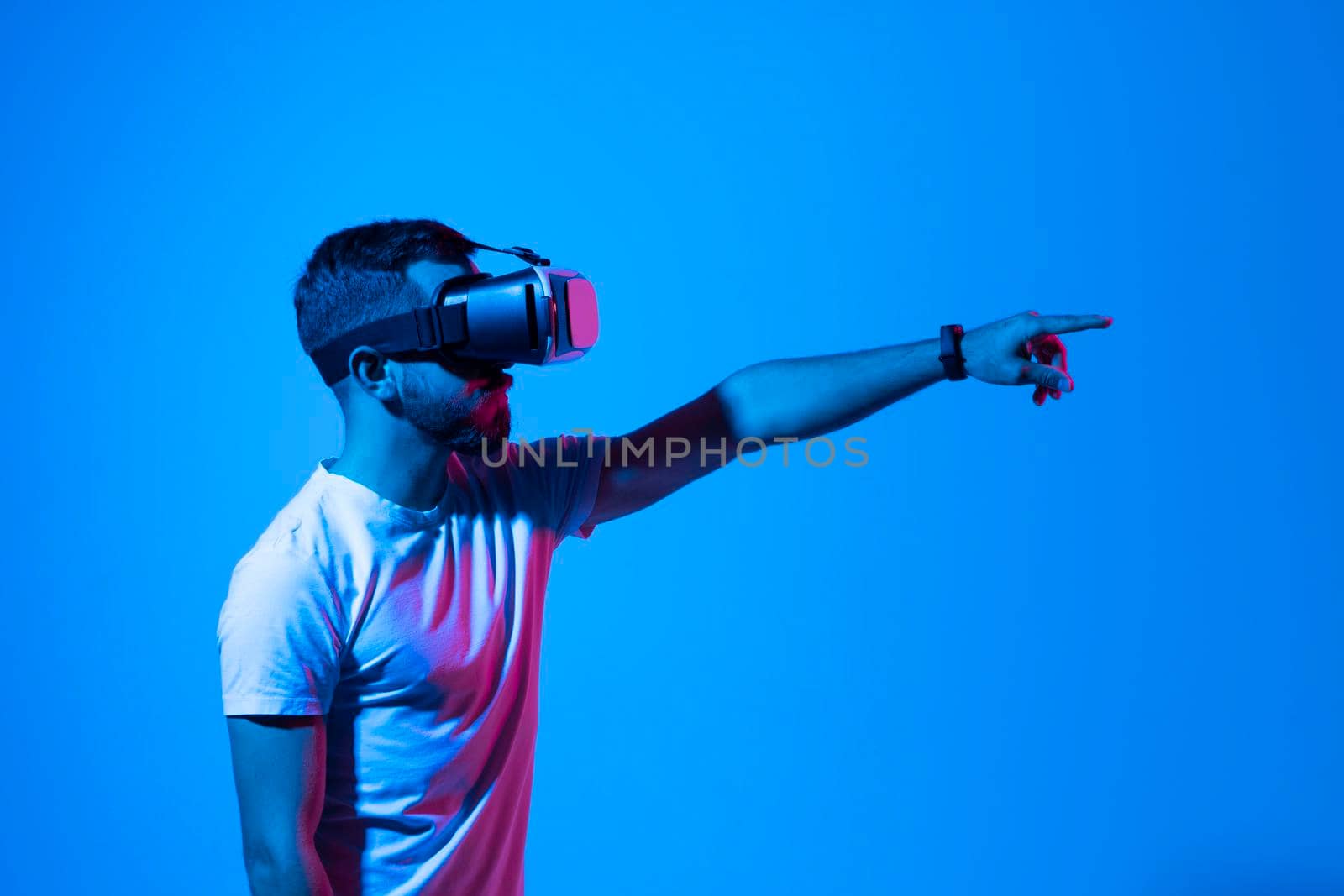 Young bearded man playing video games in VR-glasses. Excited millennial guy experiencing virtual reality while standing in neon light, copy space. by vovsht