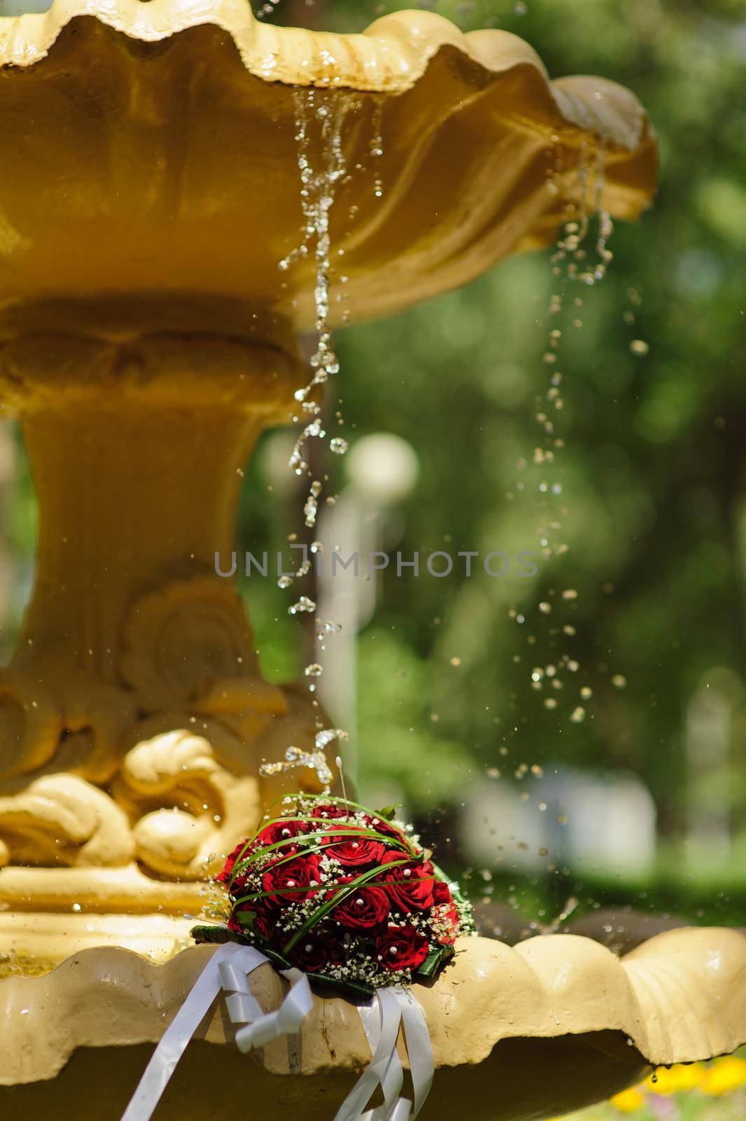 The Wedding Bouquet Of The Bride Of Red Roses Lies In An Old Fountain Under Splashes And Drops Of Water. by Andrii_Ko