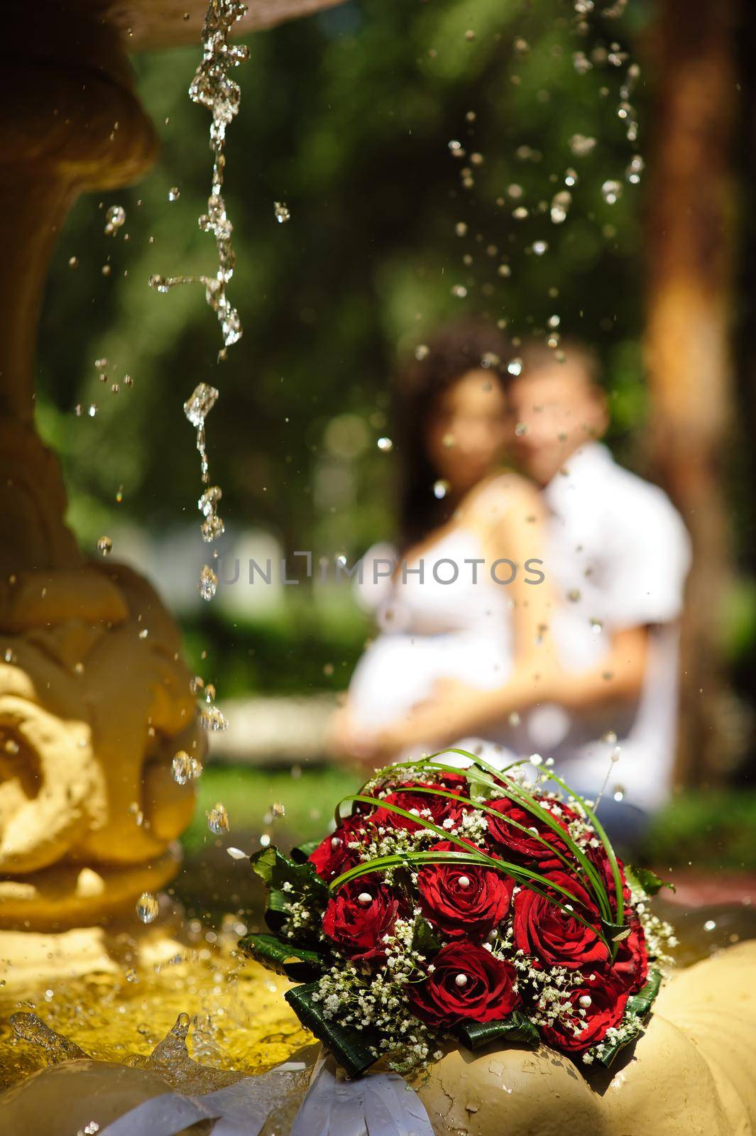 The Wedding Bouquet Of The Bride Of Red Roses Lies In An Old Fountain Under Splashes And Drops Of Water. by Andrii_Ko