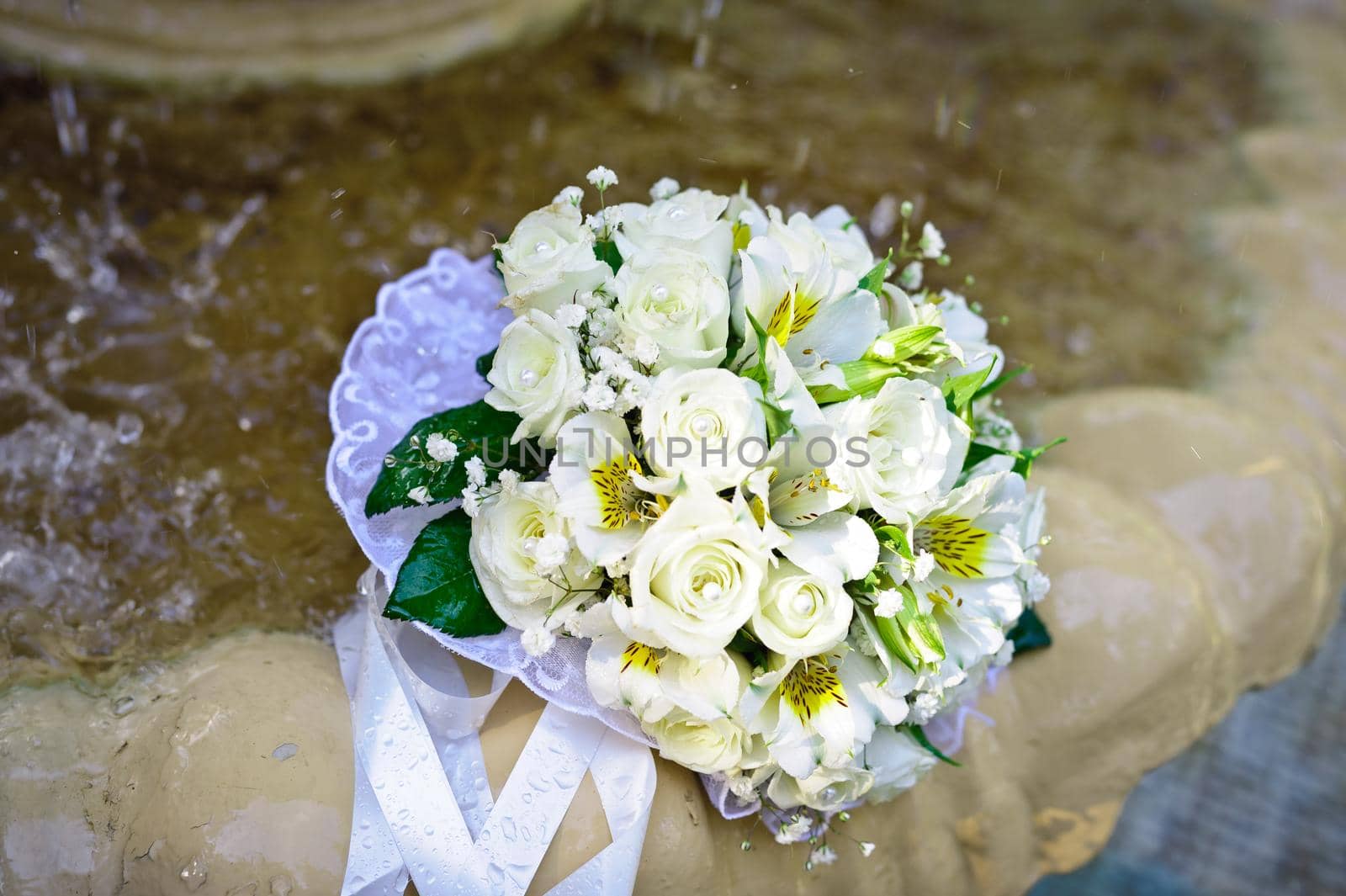 The Wedding Bouquet Of The Bride Of Red Roses Lies In An Old Fountain Under Splashes And Drops Of Water.. bridal bouquet of flowers in fountain water drops