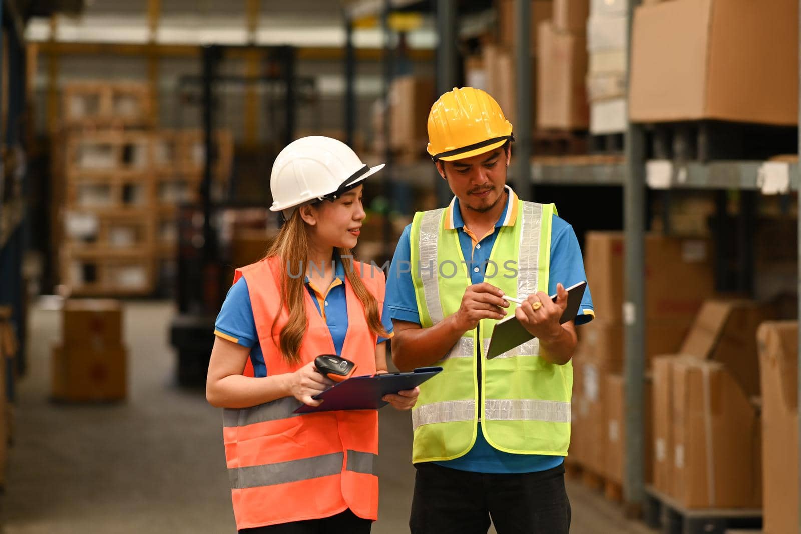 Imaged of warehouse worker standing between retail warehouse full of shelves with goods and using digital tablet.