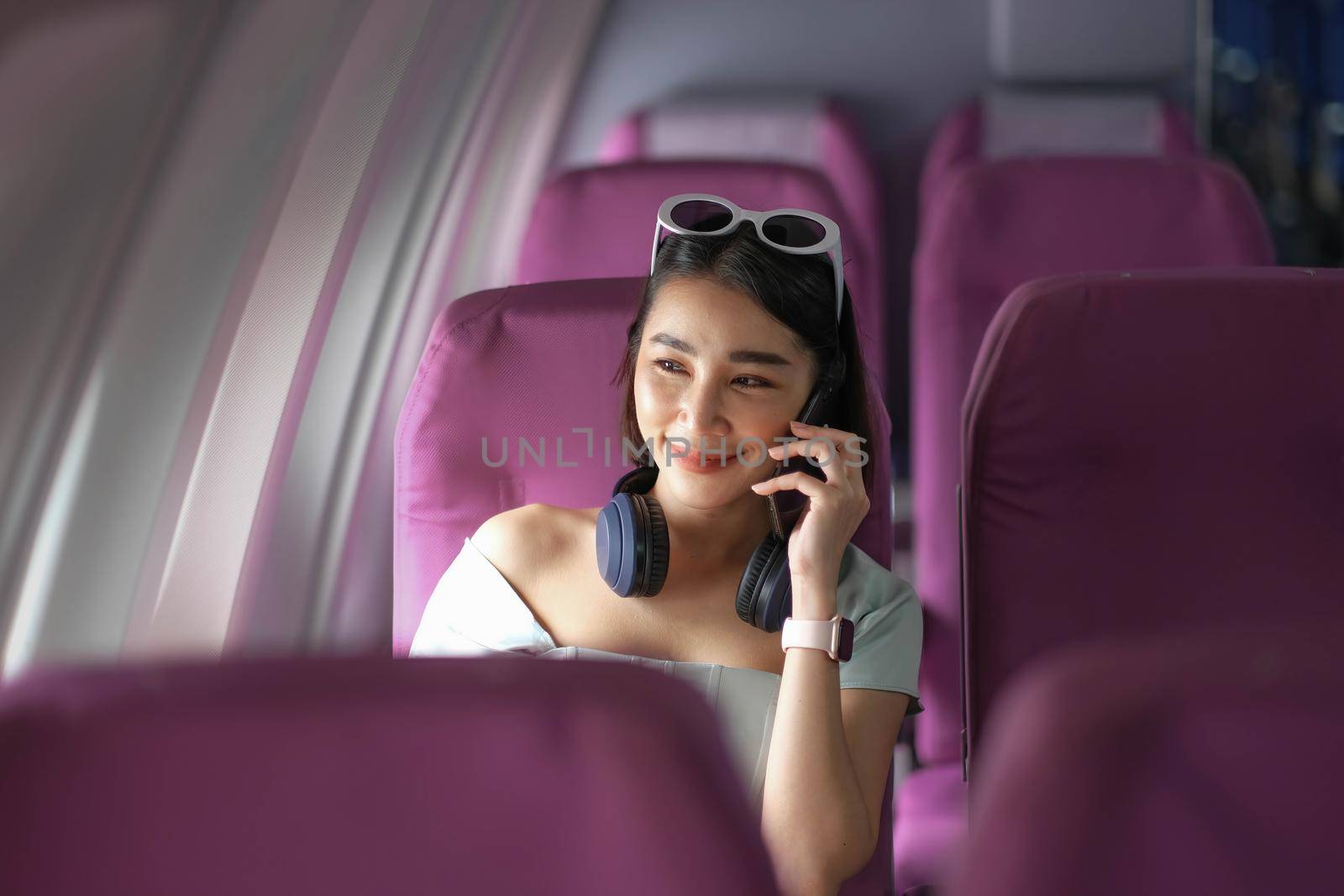 Asian woman sitting on seat in plane cabin near the window and talking on mobile phone..