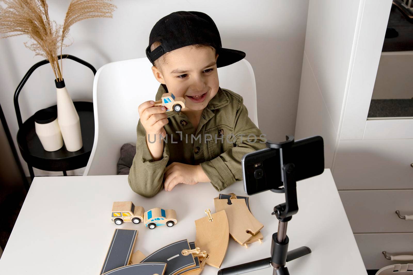 Adorable, cute, little boy blogger recording lifestyle blog, talking to camera of smartphone on tripod. Young influencer filming vlog for his channel. Child makes video for his followers online